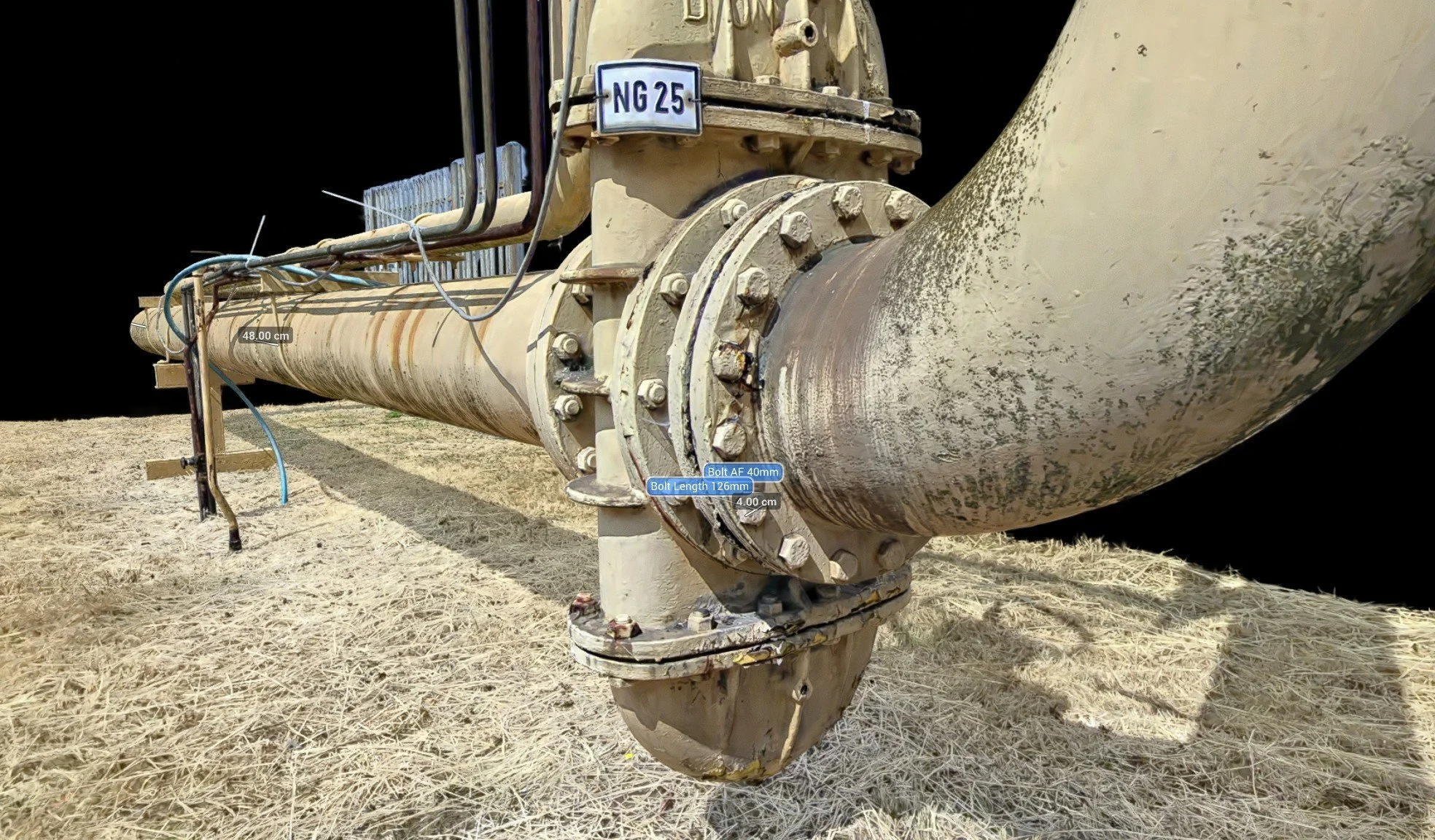 Close-up of a large industrial pipe with several labeled measurements and a wheel mechanism, situated outdoors on dry grass.