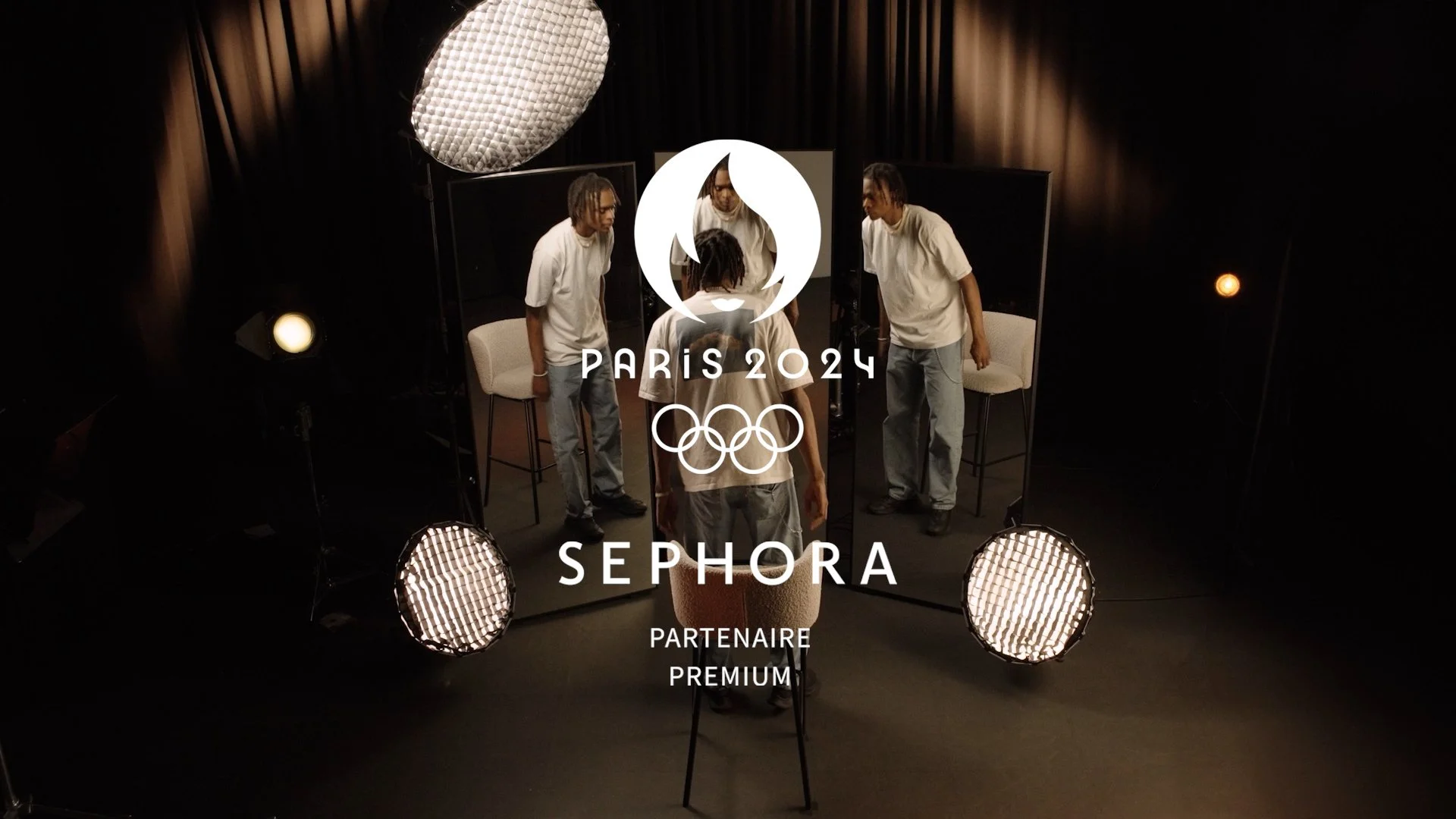 Photo en studio avec trois personnes regardant leur reflet dans un miroir au centre, éclairage professionnel, logo des Jeux Olympiques de Paris 2024, partenariat avec Sephora, ambiance sombre