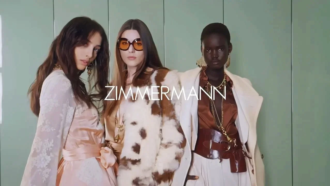 Trois femmes posant devant un mur vert, portant des vêtements élégants, avec le logo ZIMMERMANN.