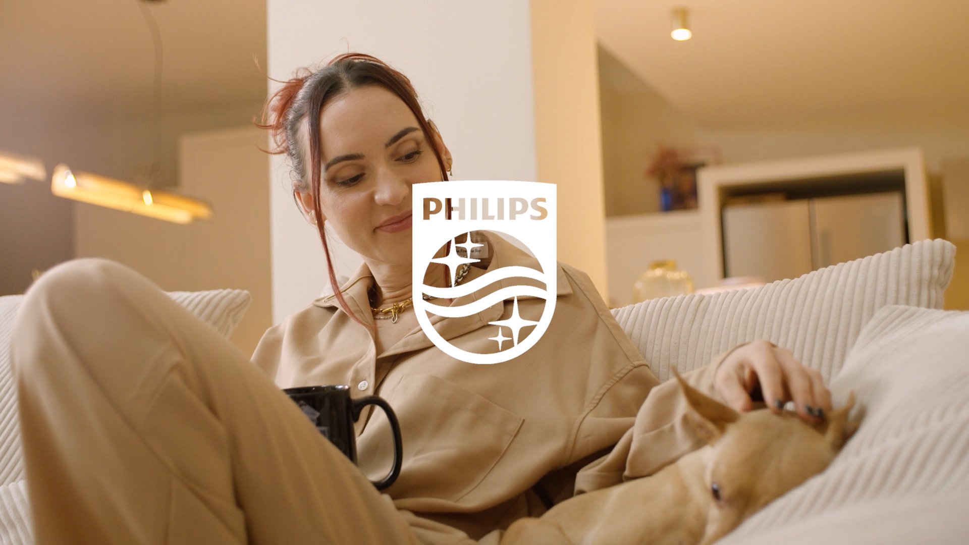 Une femme assise sur un canapé en train de regarder quelque chose, avec le logo Philips en superposition.