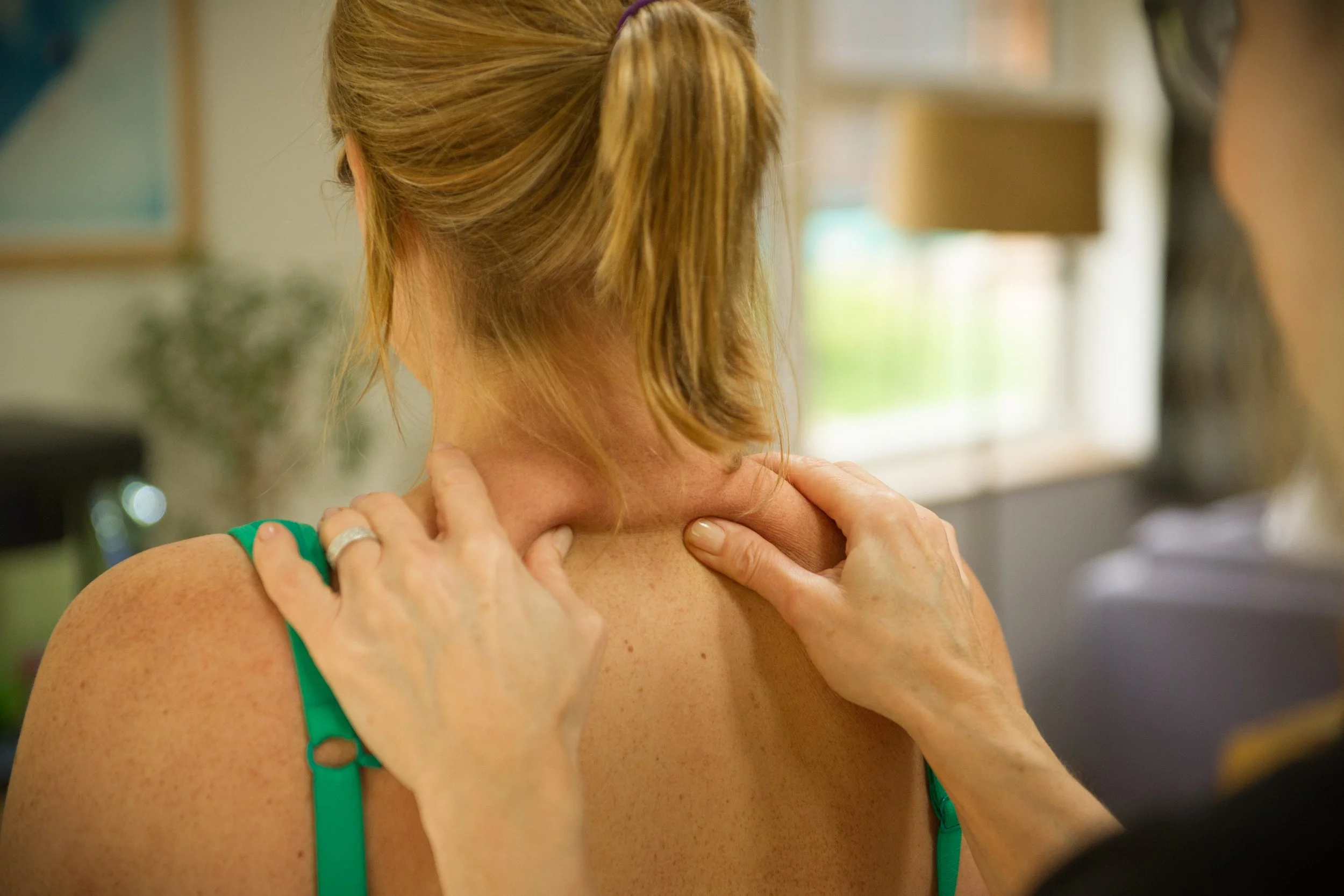 A woman receiving an acupuncturist treatment on her neck and shoulder in a clinic setting.
