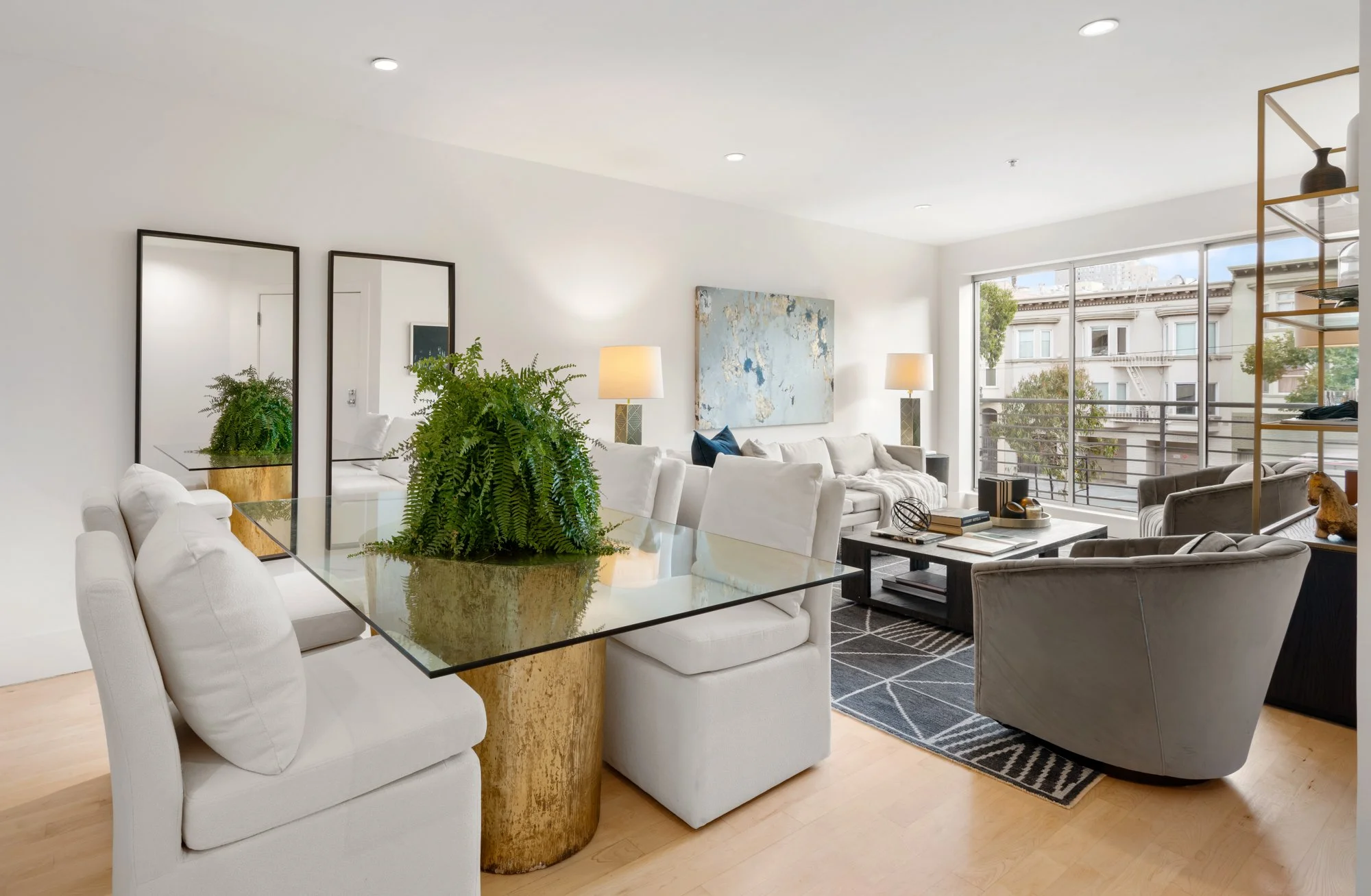 Modern living room with white walls, large window, beige sofas, gray and black armchair, coffee table, decorative items, and green plants.