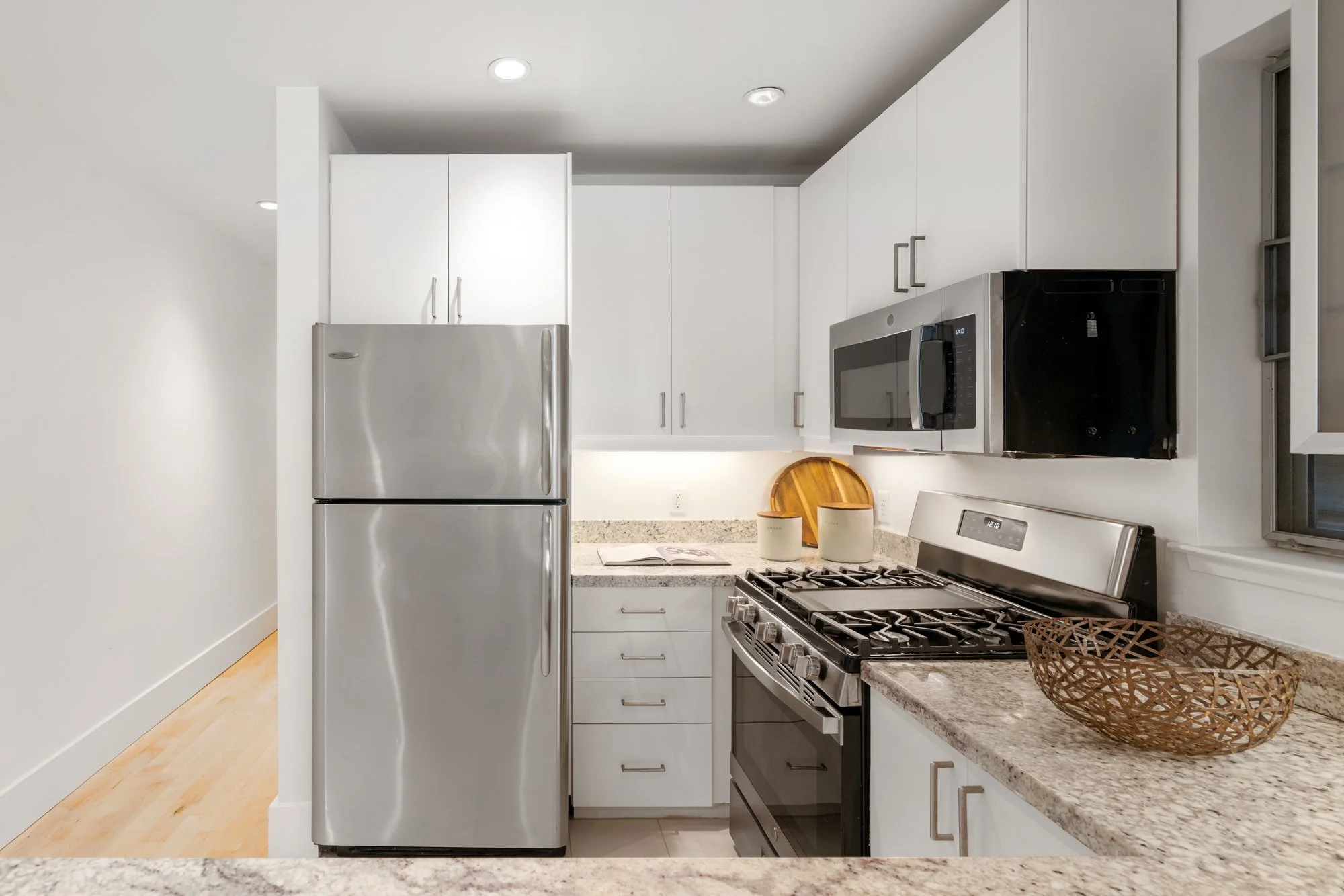 Modern kitchen with stainless steel refrigerator, black stove, microwave, white cabinets, granite countertop, and decorative items.
