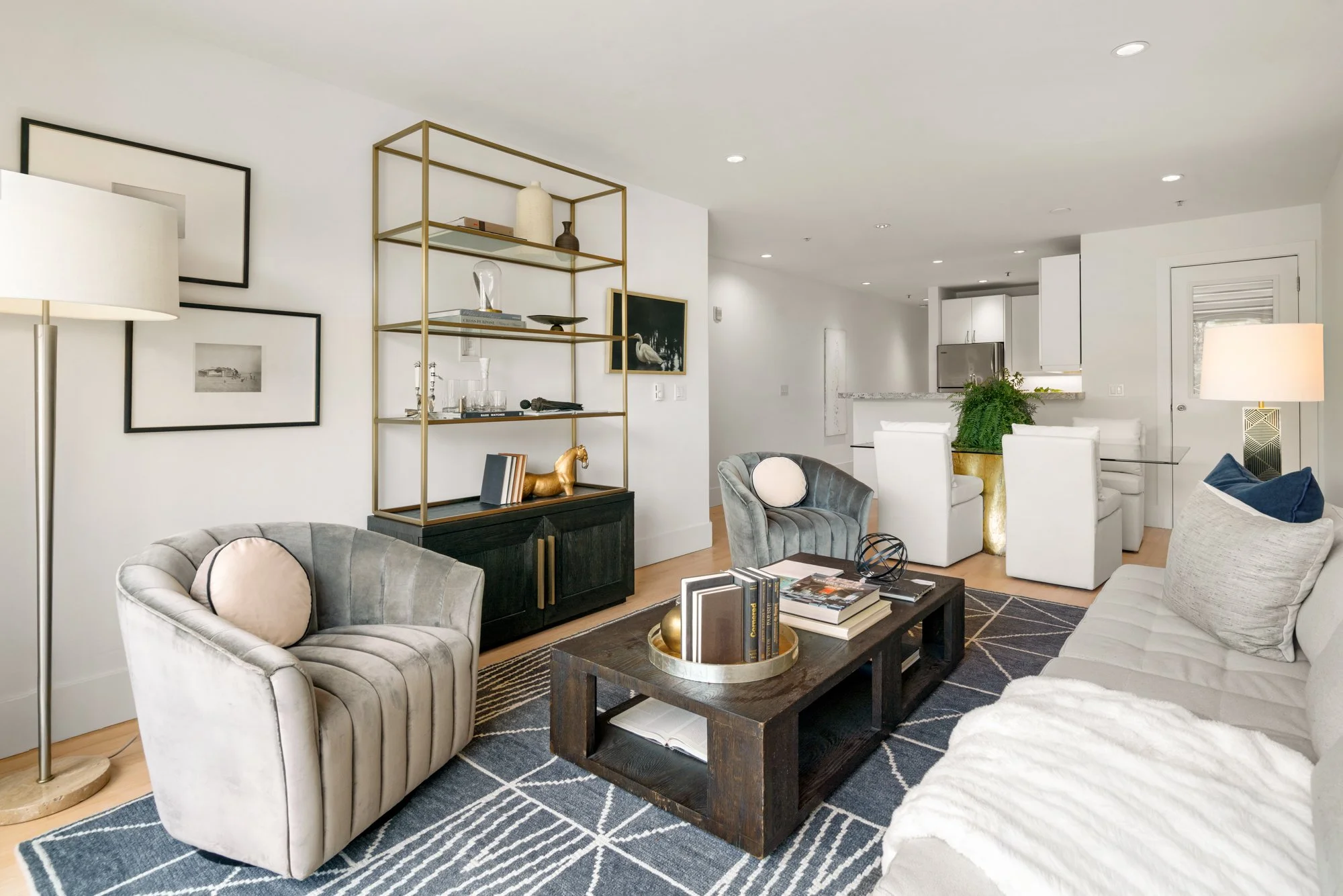 Modern living room with gray and white furniture, a black coffee table, a gold bookshelf, and decorative items.