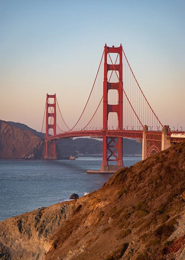 Golden Gate Bridge in San Francisco during sunset, viewed from a rocky hillside.