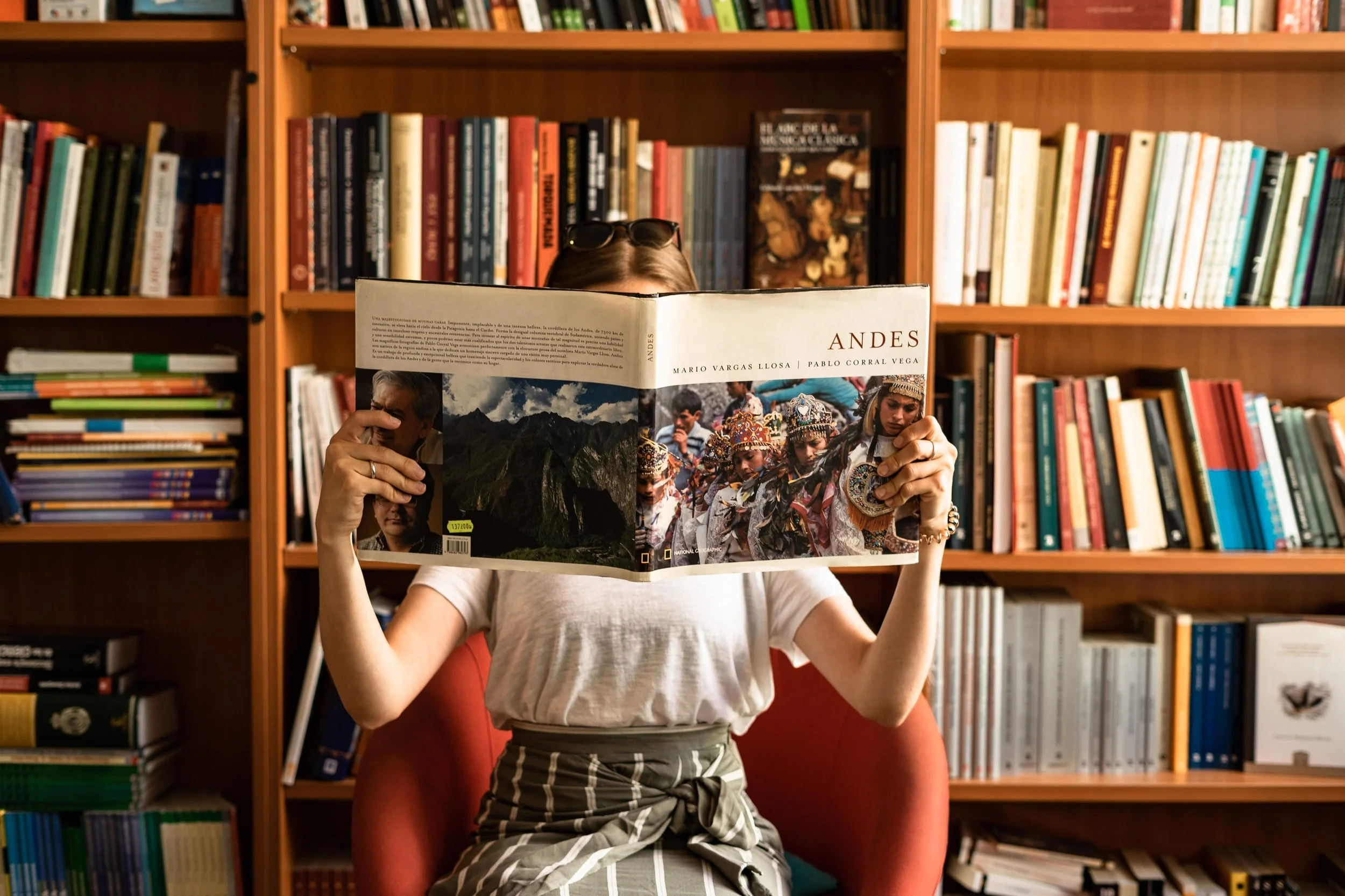 A person reading a large book in a library filled with bookshelves.