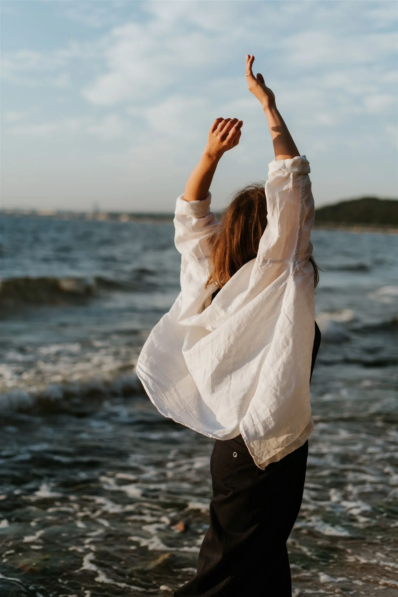 A woman dancing at sunset with her arms raised.