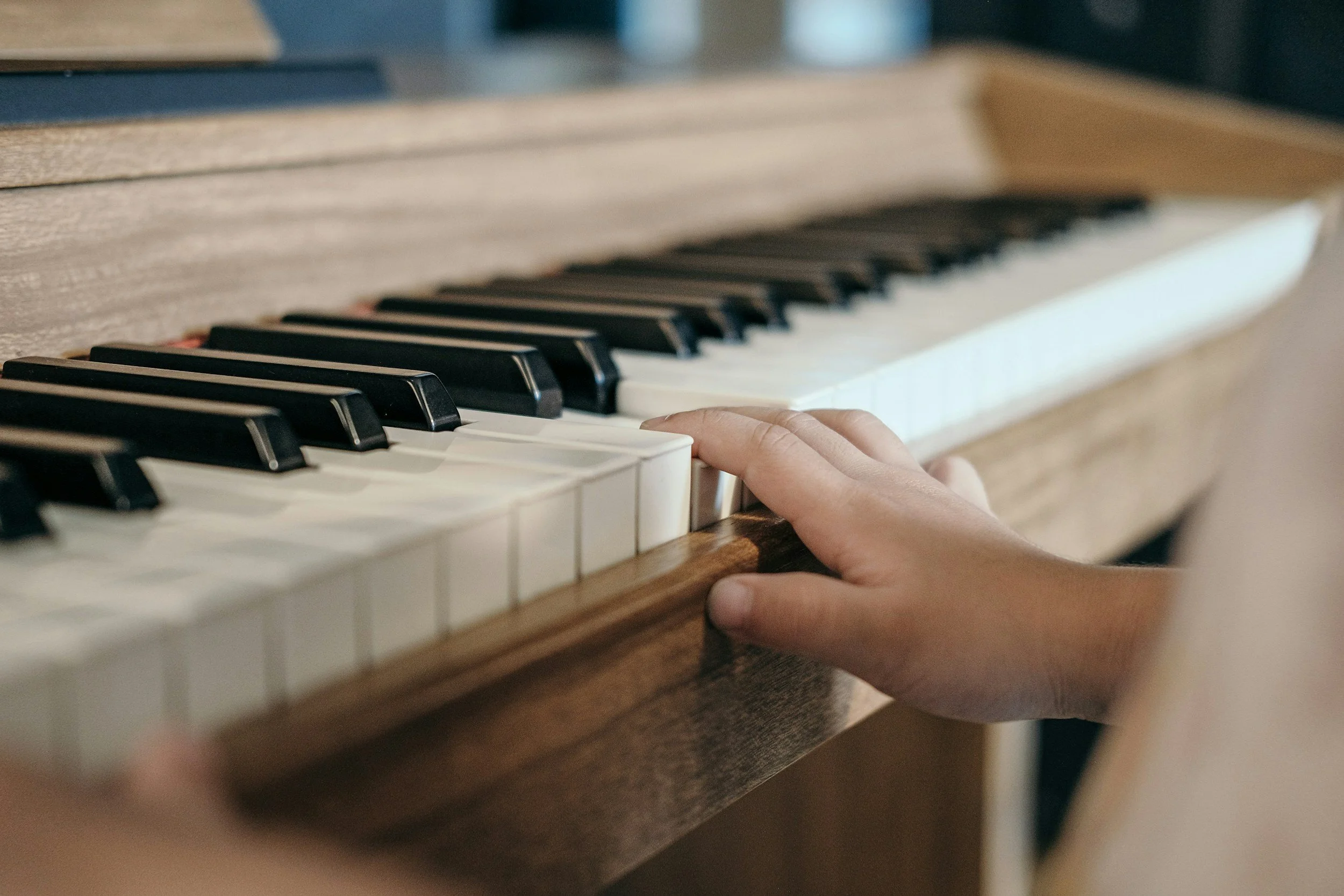 A person's hand playing the keys of a wooden piano, with black and white keys visible.
