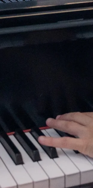 A person playing a black piano, with their hand on the keys.
