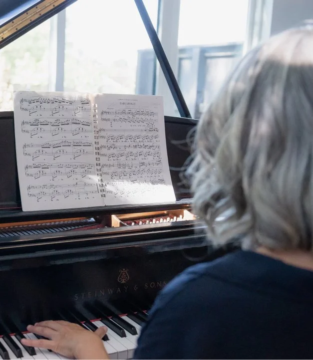 A person playing a grand piano, with sheet music placed on the music stand.