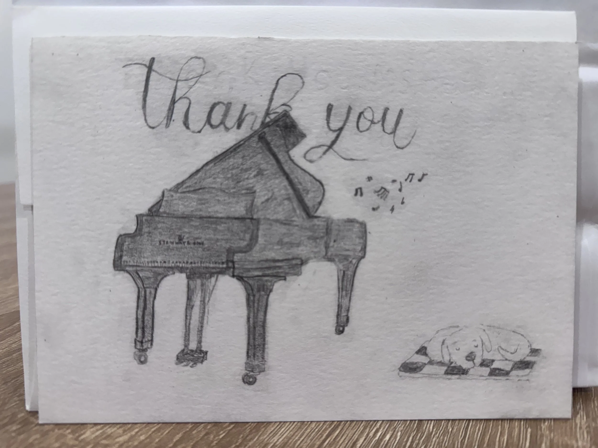 A hand-drawn thank you card featuring a grand piano with music notes and a small dog lying on a checkered blanket.