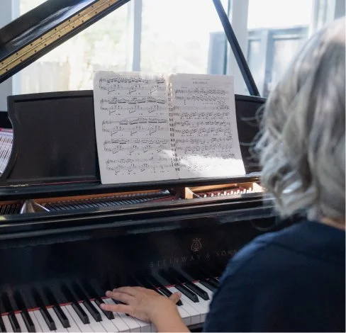 Child playing a grand piano with sheet music on the music stand.