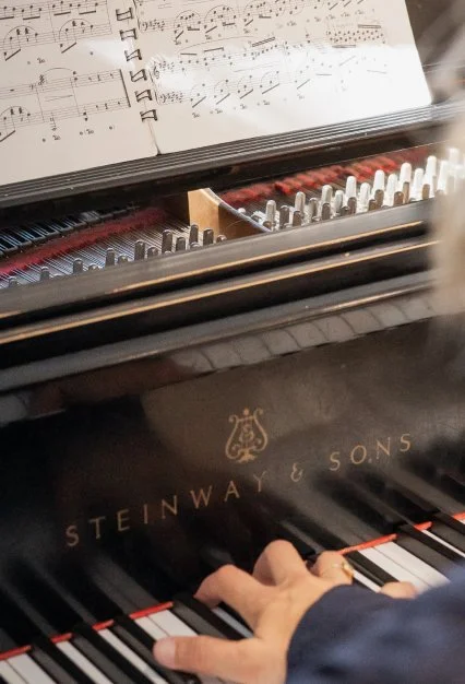 Close-up of a piano with a person's hand playing the keys, sheet music open on the music stand.