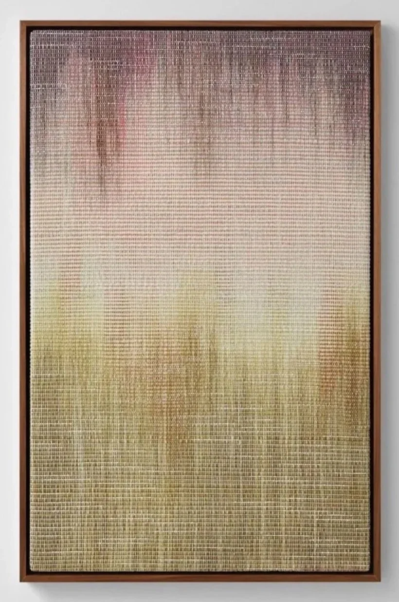 A woven piece of artwork with a wooden frame, featuring a grid pattern with varying shades of beige, brown, and purple.