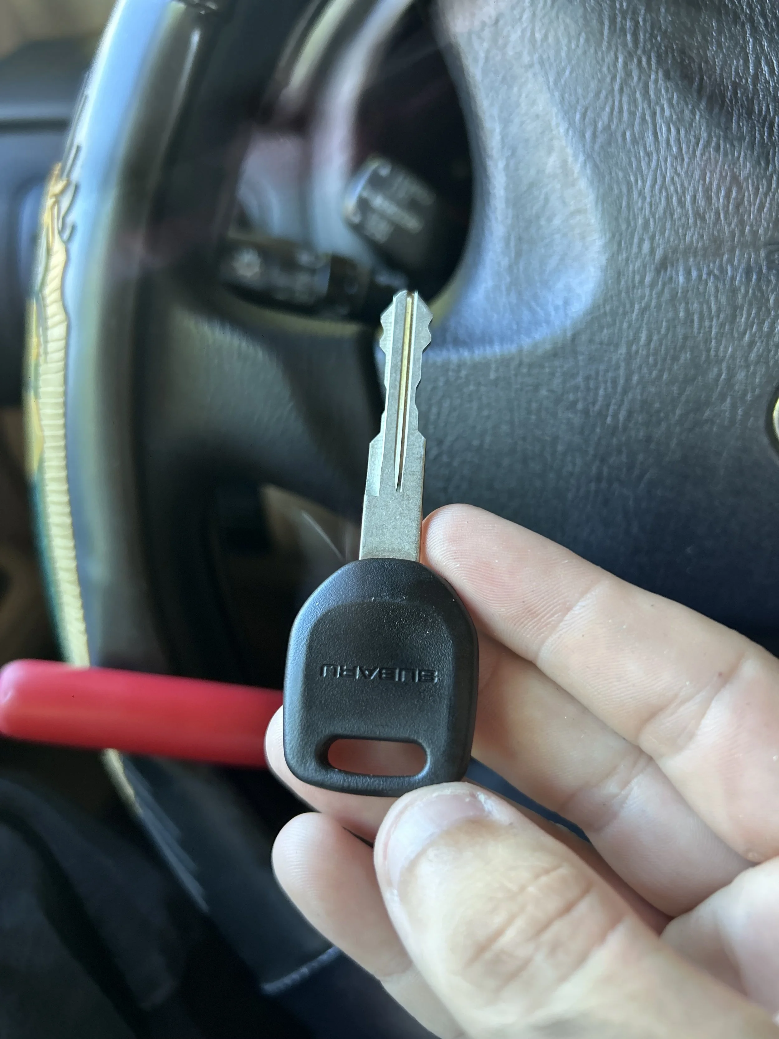 A person holding a car key with a black plastic head near a car's ignition switch, inside a vehicle.