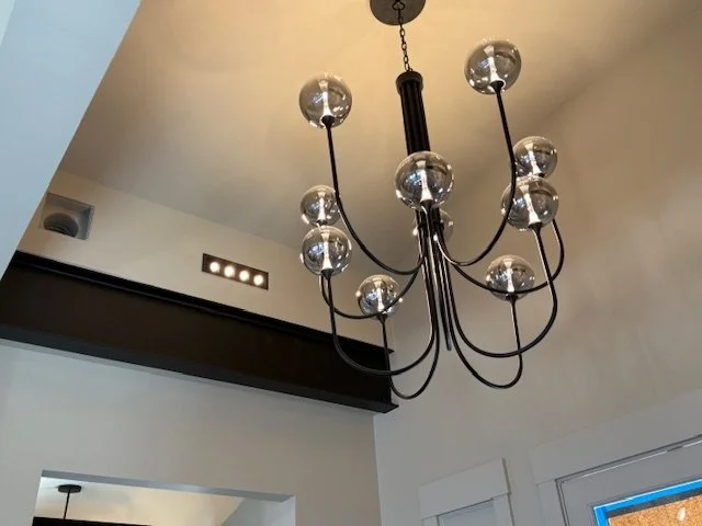 Black chandelier with glass globes hanging from a white ceiling in a modern room.