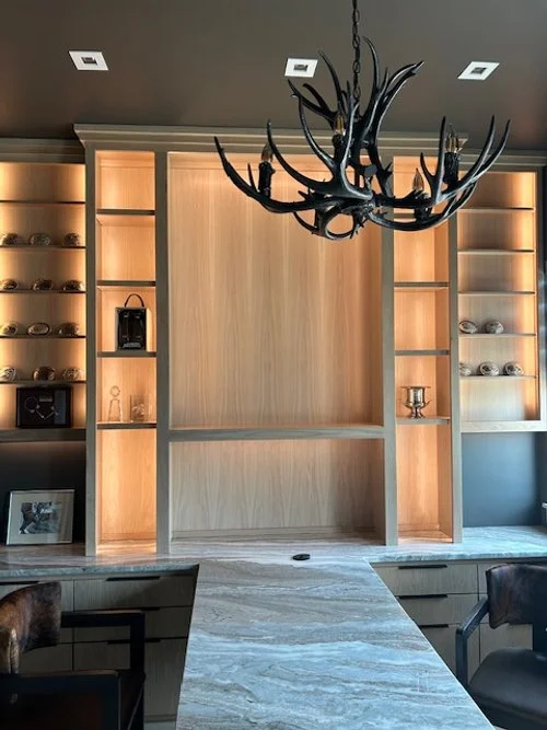 Modern built-in wooden shelves with decorative items and a central empty space, accented by a black antler chandelier hanging from the ceiling.