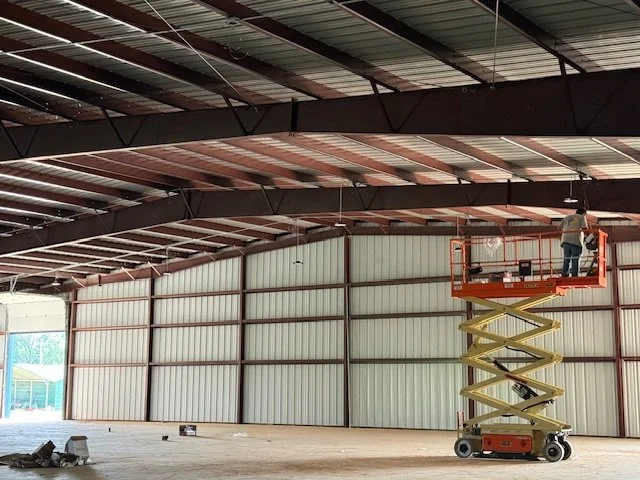 Worker on orange scissor lift inside a large industrial warehouse, installing or inspecting ceiling panels.