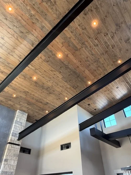 Interior view of a modern building with a wooden ceiling, recessed lighting, and black metal beams.