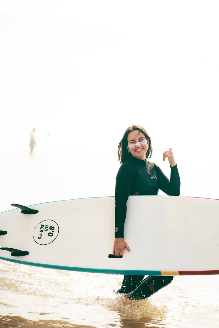 Frau mit Surfbrett im Wasser, lachend, bei sonnigem Wetter