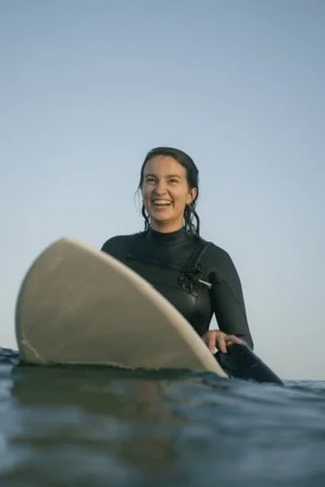Eine junge Frau beim Surfen im Wasser, lächelnd und glücklich.