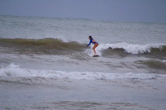 Eine Person beim Surfen auf einer Welle im Meer bei bewölktem Himmel.
