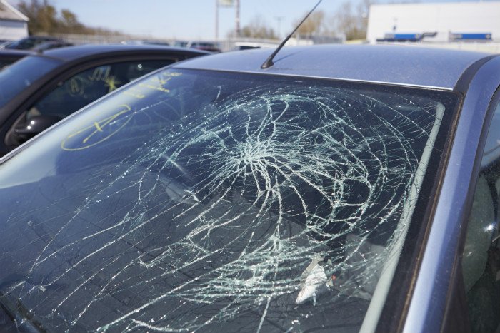 A car with a cracked windshield in a parking lot, with other vehicles visible in the background.