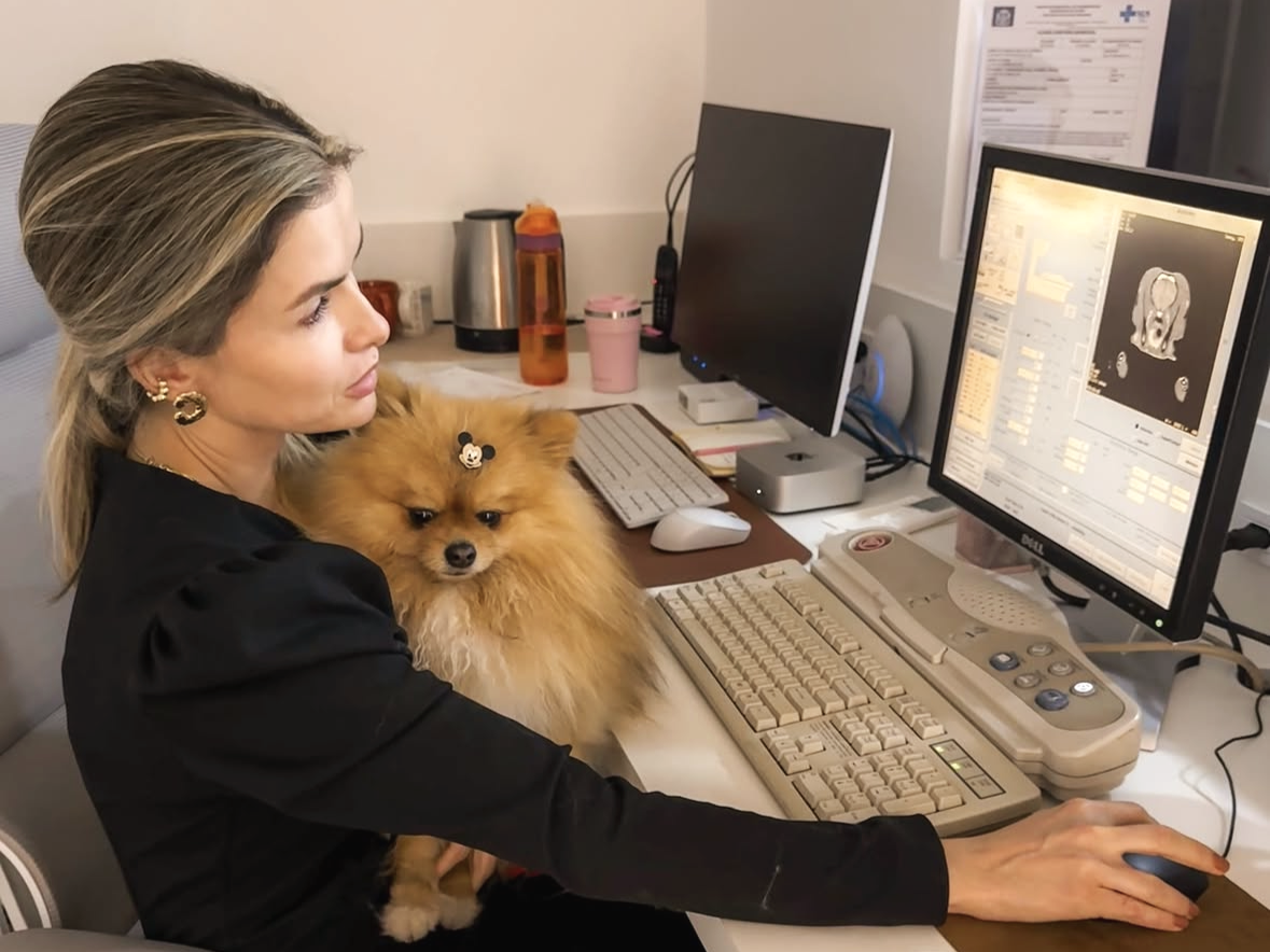 Mulher no escritório segurando um cão de raça Spitz enquanto olha monitor com imagens de exame médico.