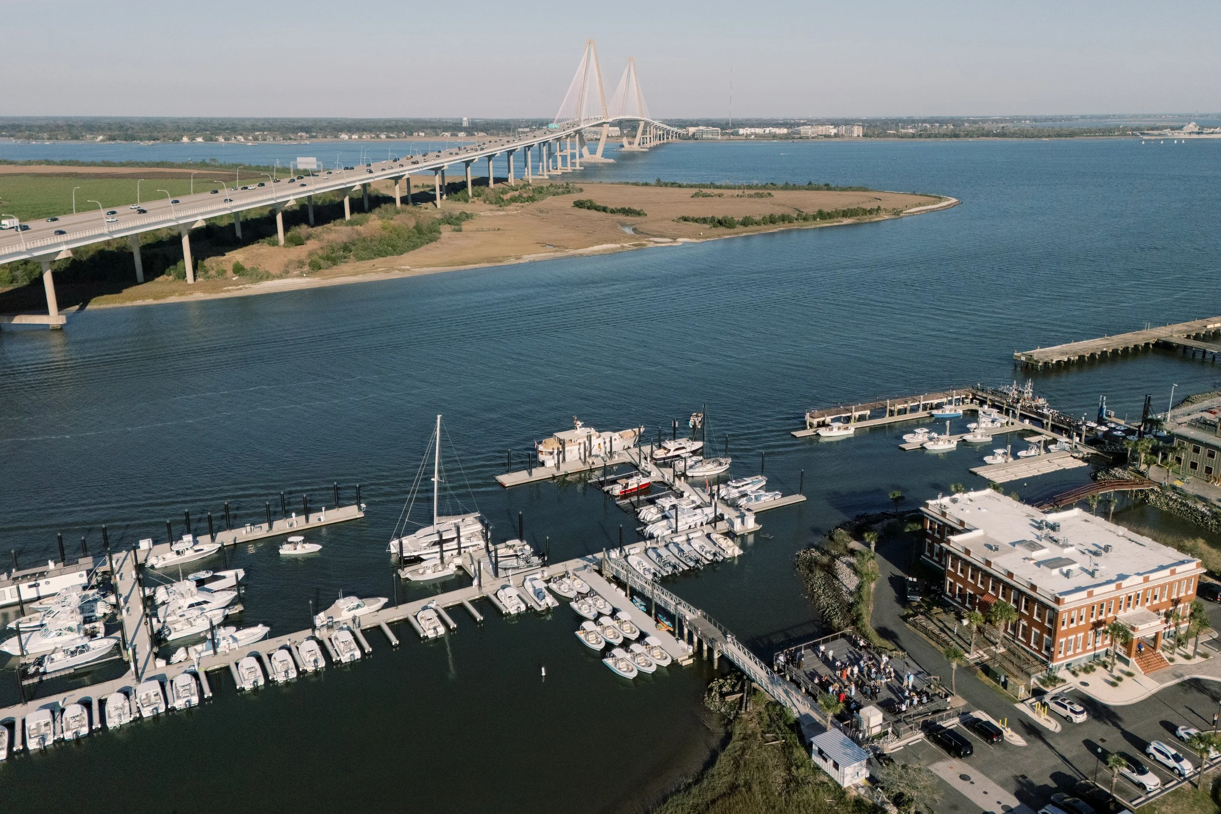 Aerial view of a marina with boats docked, a city skyline in the background, a large bridge over a river, and downtown buildings on the horizon.