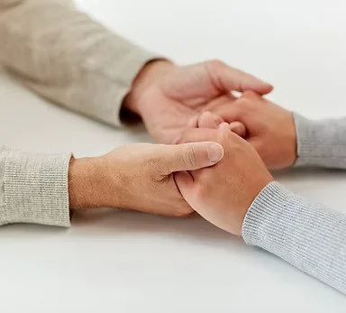 Two people holding hands on a table, one with a light-colored sweater and the other with a gray sweater.