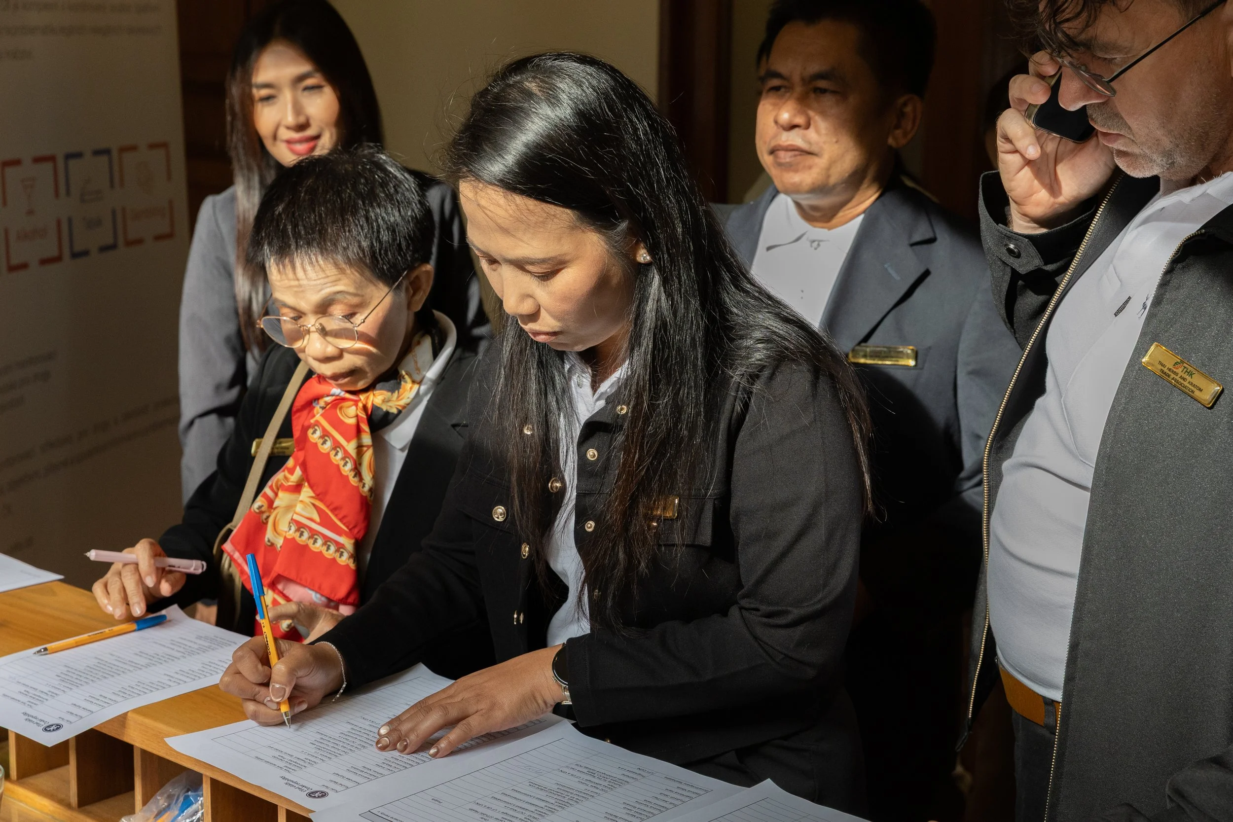 Group of five people, three women and two men, signing documents at a wooden counter in an indoor setting.