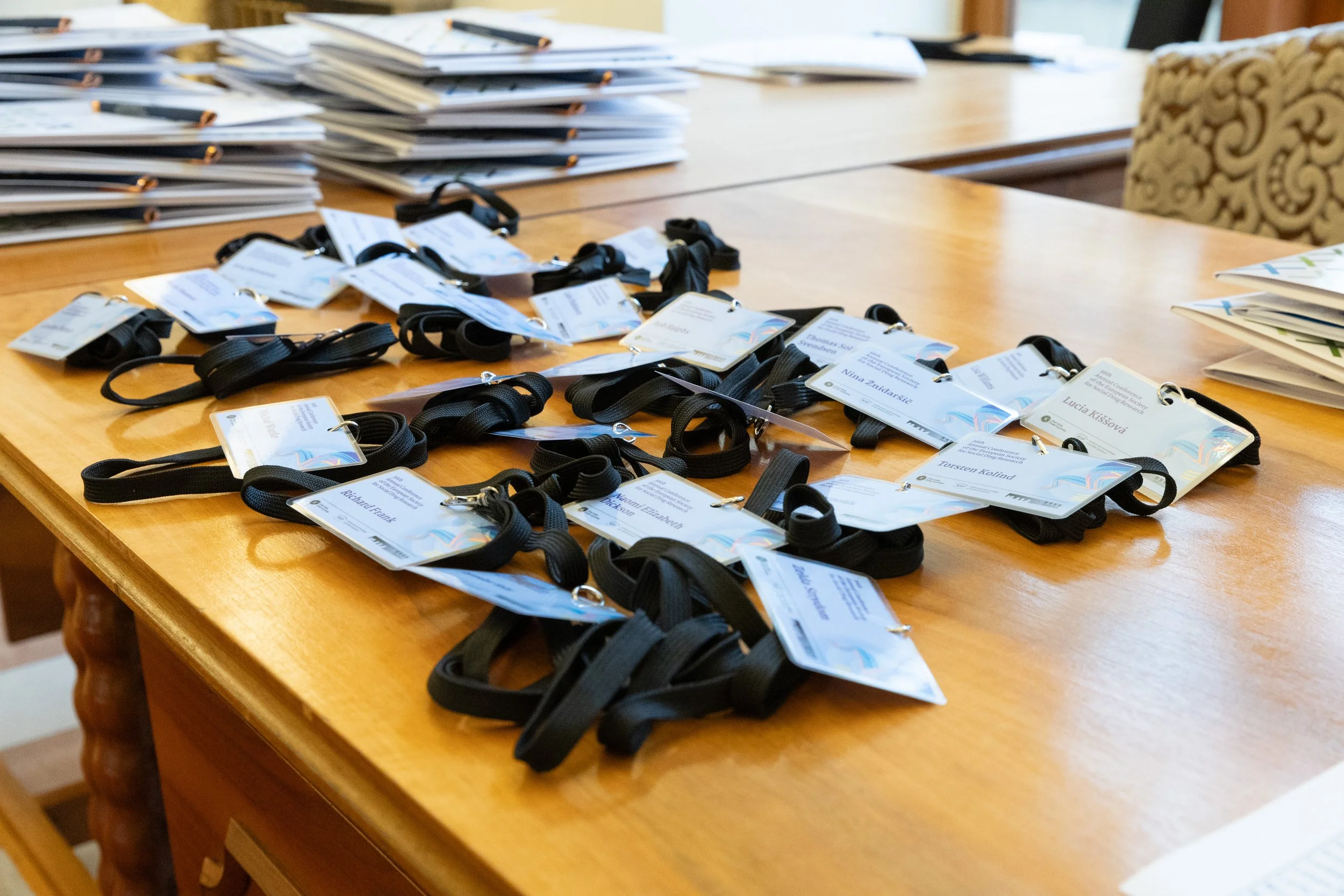 Name badges with black lanyards and stacks of papers on a wooden conference table.