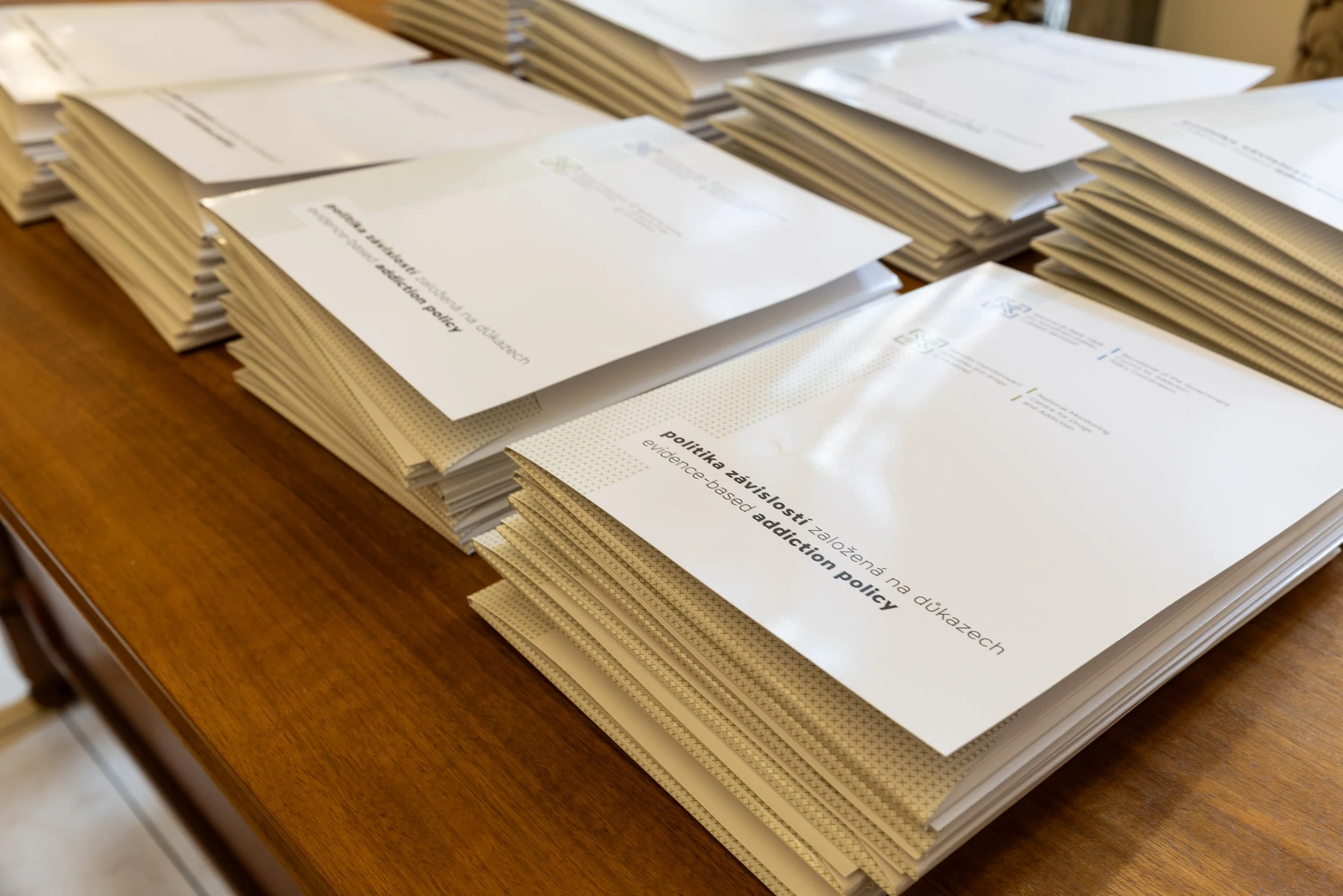 Stacks of papers on a wooden table with visible text including 'evidence-based addiction policy' and 'Política zwiąłosci na złozonych na edukazach'.