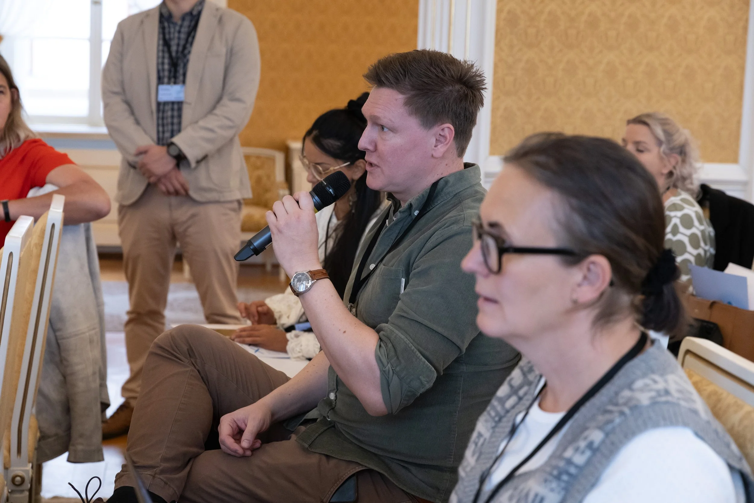 A man sitting in a conference room speaking into a microphone during a discussion or presentation.
