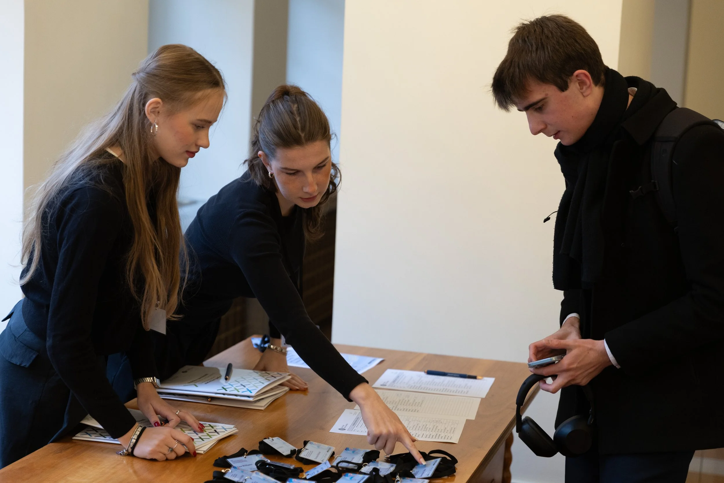 Three young adults at a conference registration table examining name tags and registration materials.