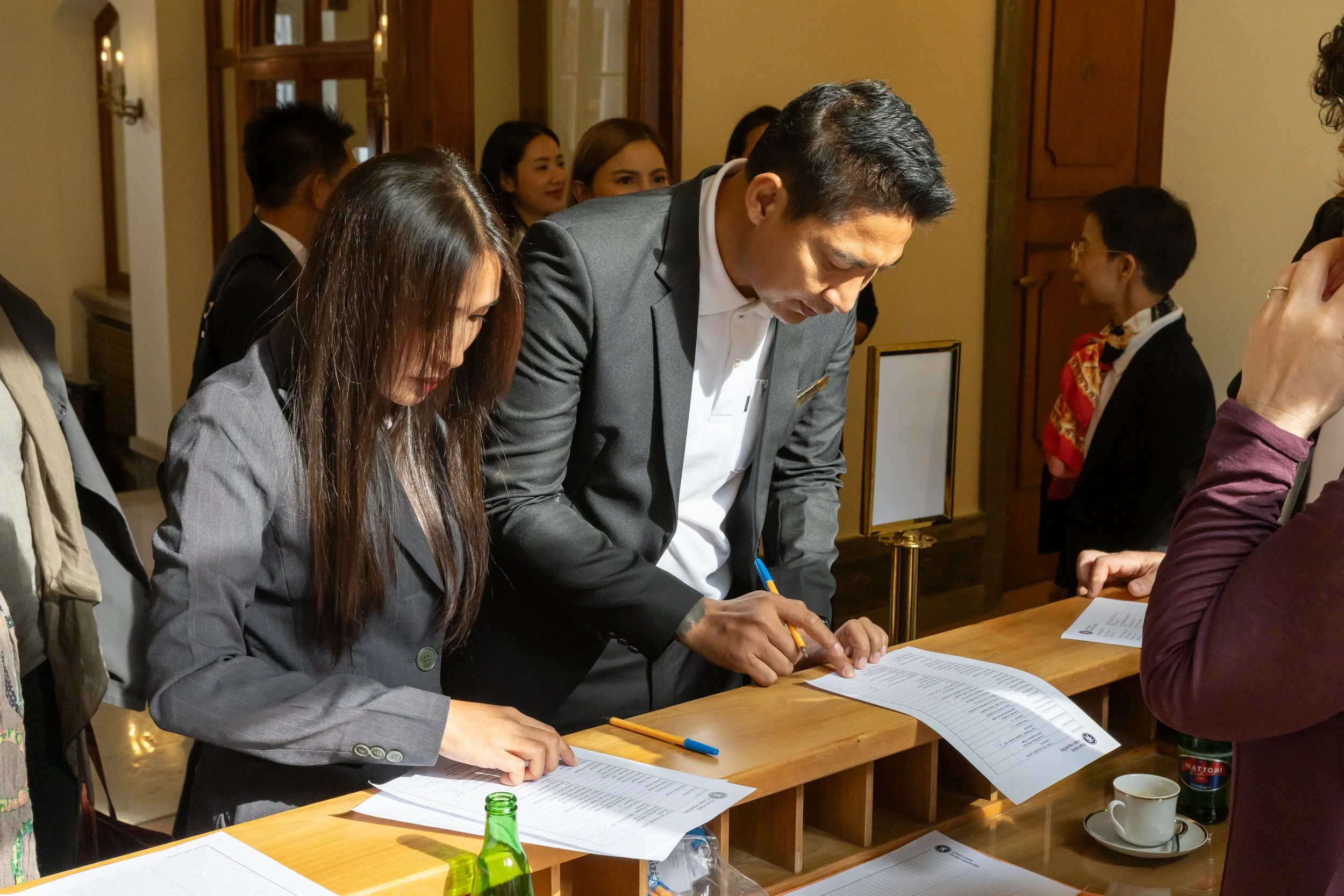 People signing documents at a reception desk in a formal setting.