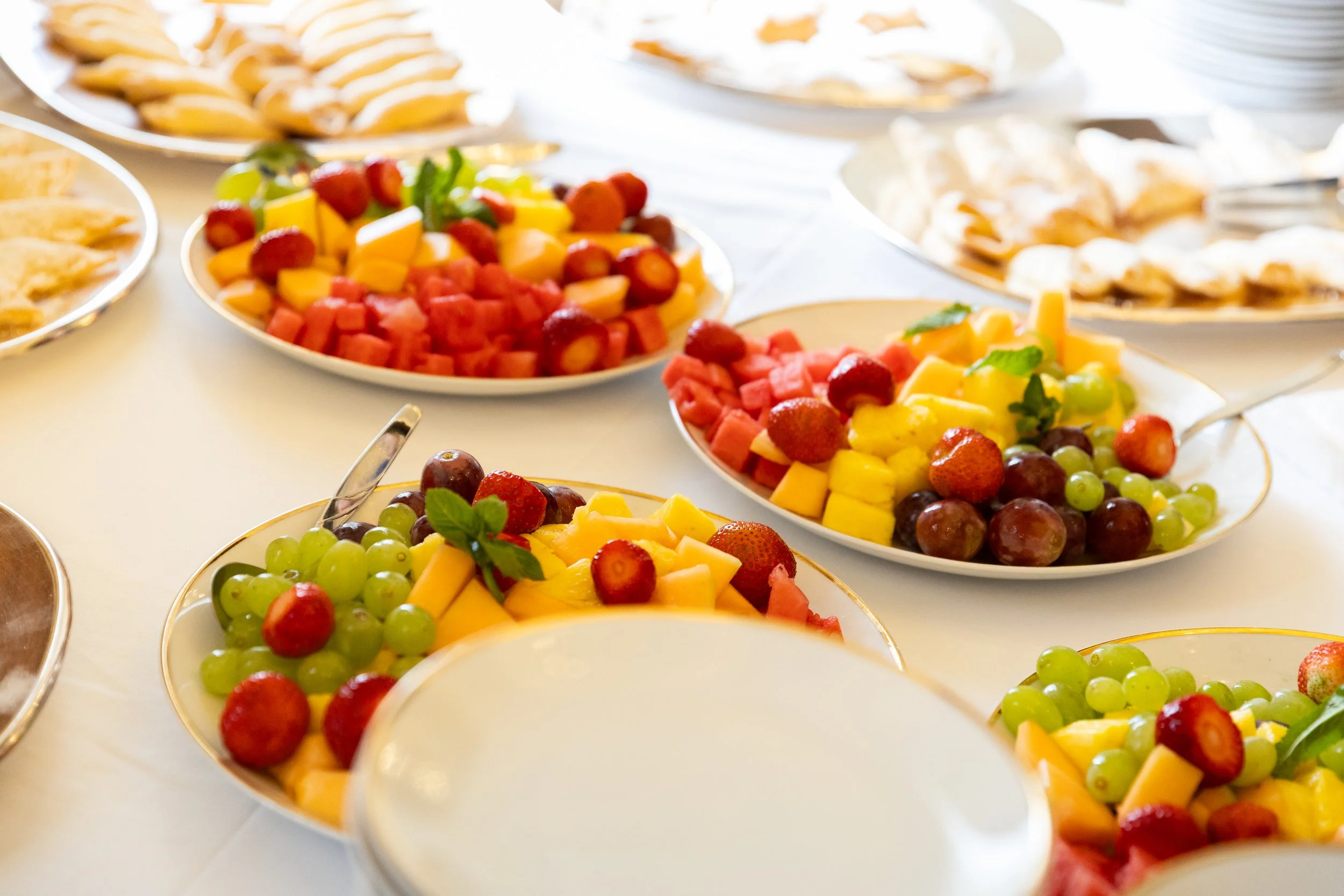 Fruit salad trays with grapes, watermelon, strawberries, mango, and honeydew on a banquet table.