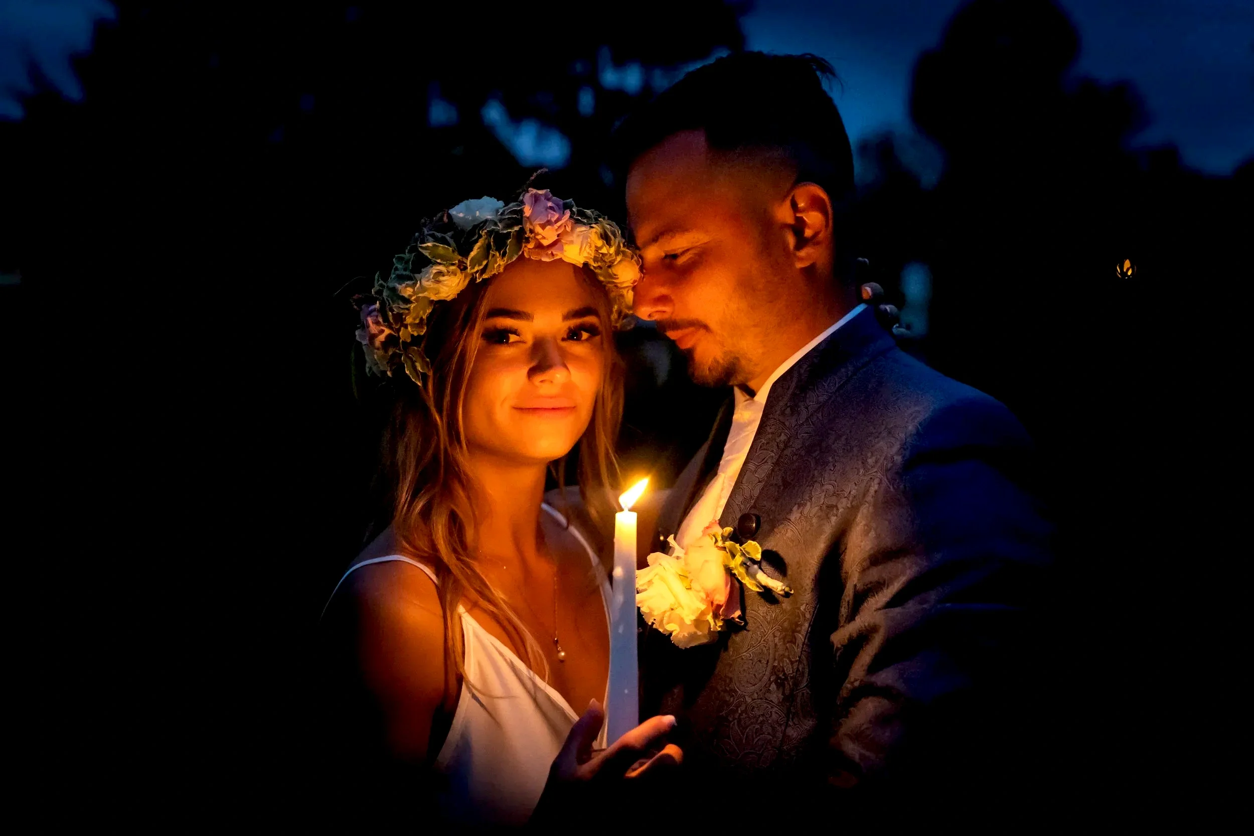 A bride and groom holding a candle together during their wedding at night.