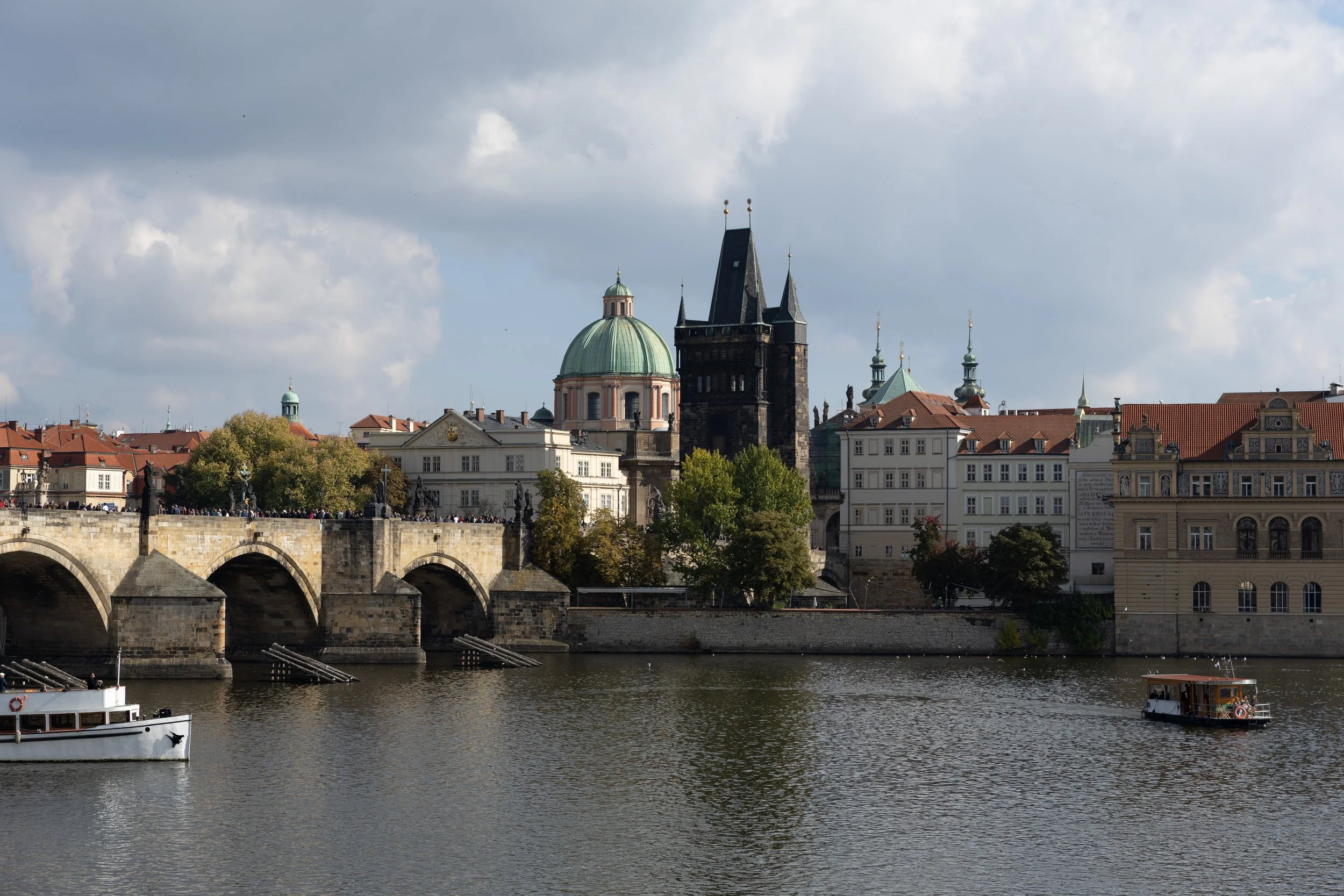 View of Prague skyline with historic buildings and a river with boats.