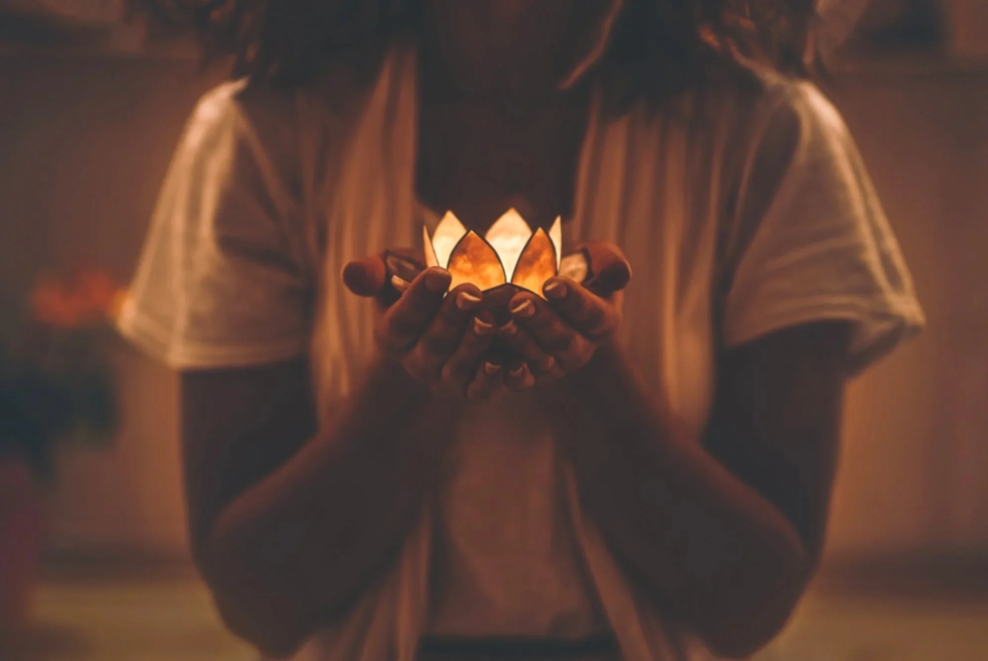 Person holding a lit decorative candle in the shape of a lotus flower.