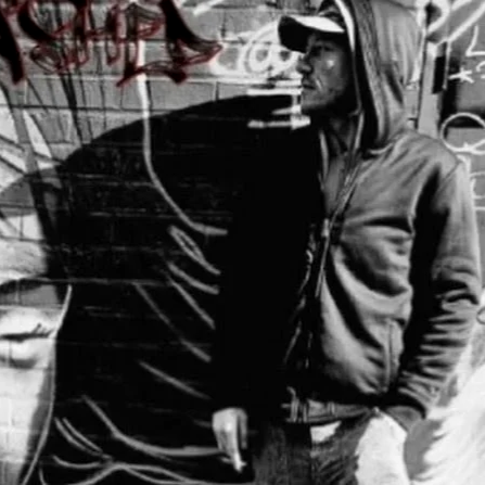 A young man in a hoodie and baseball cap standing next to a graffiti-covered wall.