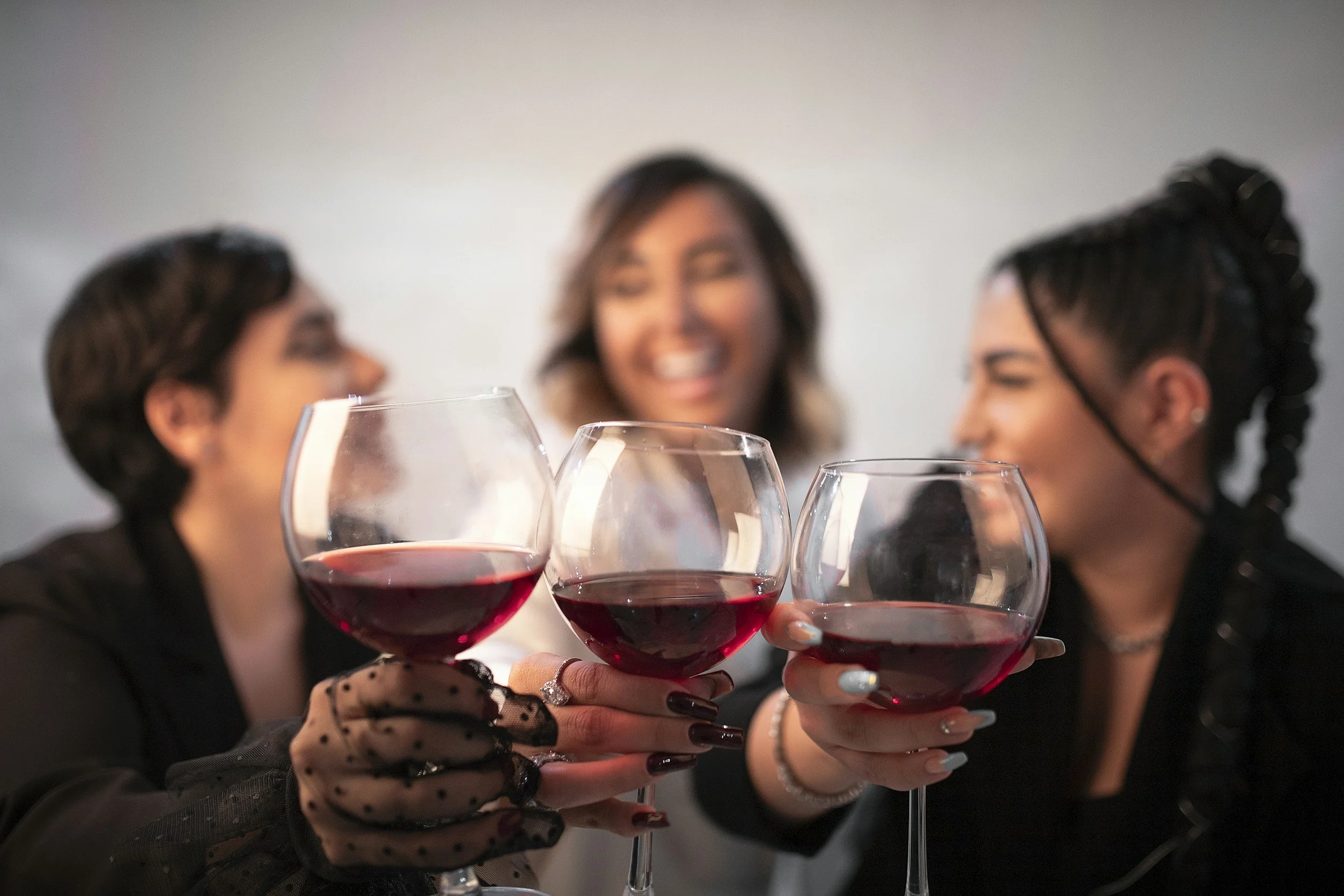Three women clinking glasses of red wine, smiling and celebrating together, in focus, with a blurred background.