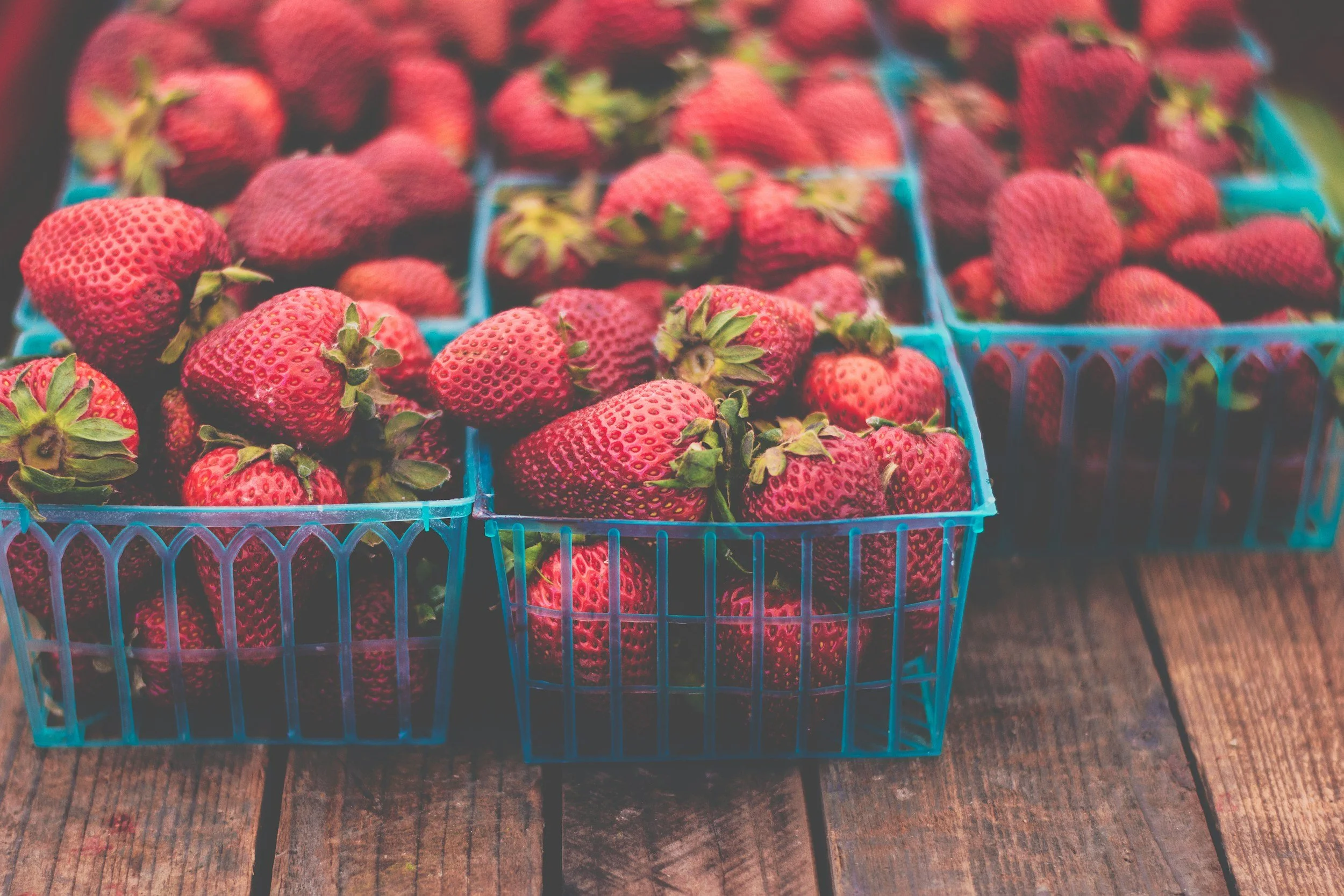 Baskets of fresh strawberries on a wooden surface.