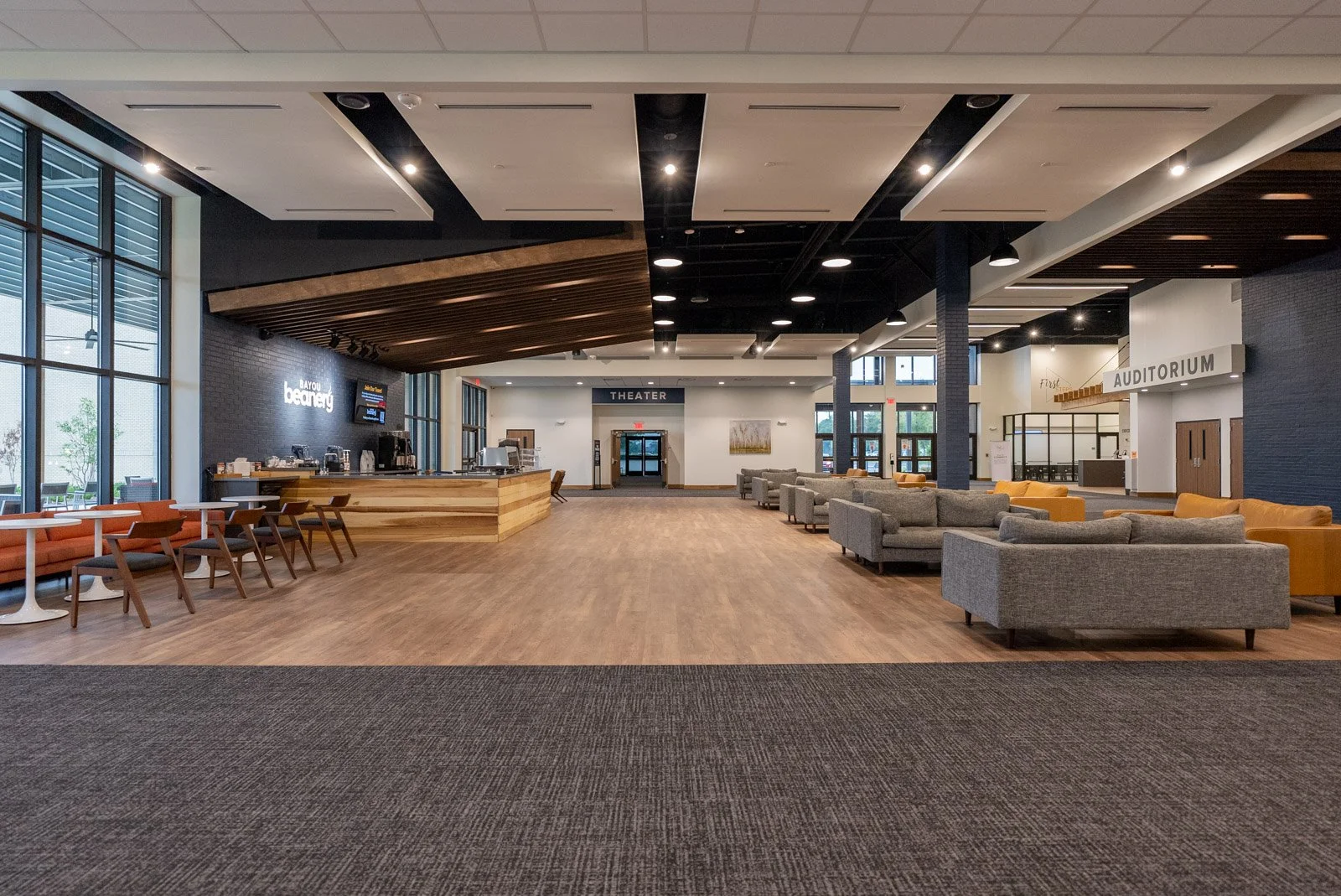 Wide view of a modern building lobby with seating, a coffee counter, and signs indicating a theater and auditorium.