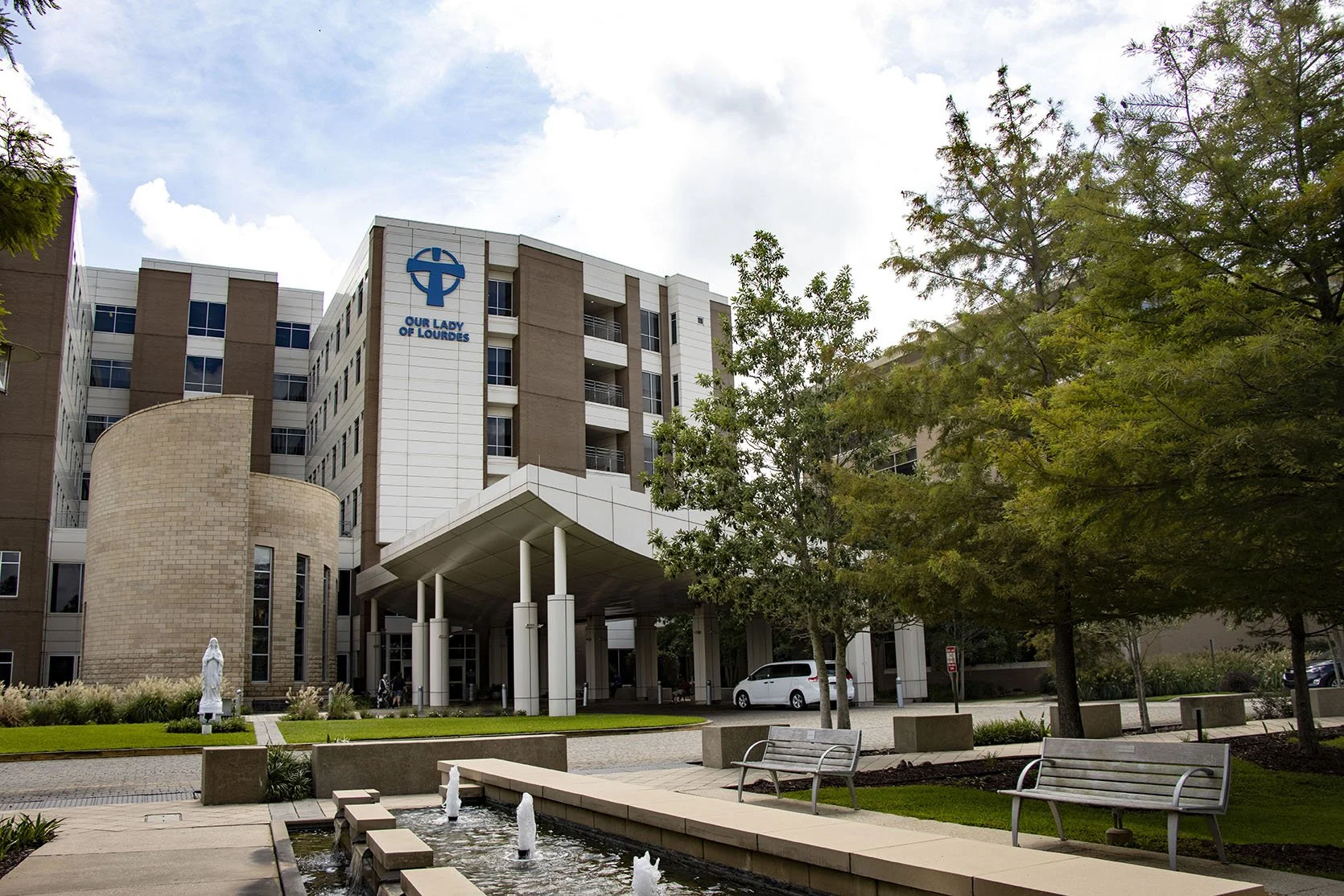 Main entrance of Our Lady of Lourdes Regional Medical Center with fountain, statue, and landscaped grounds.