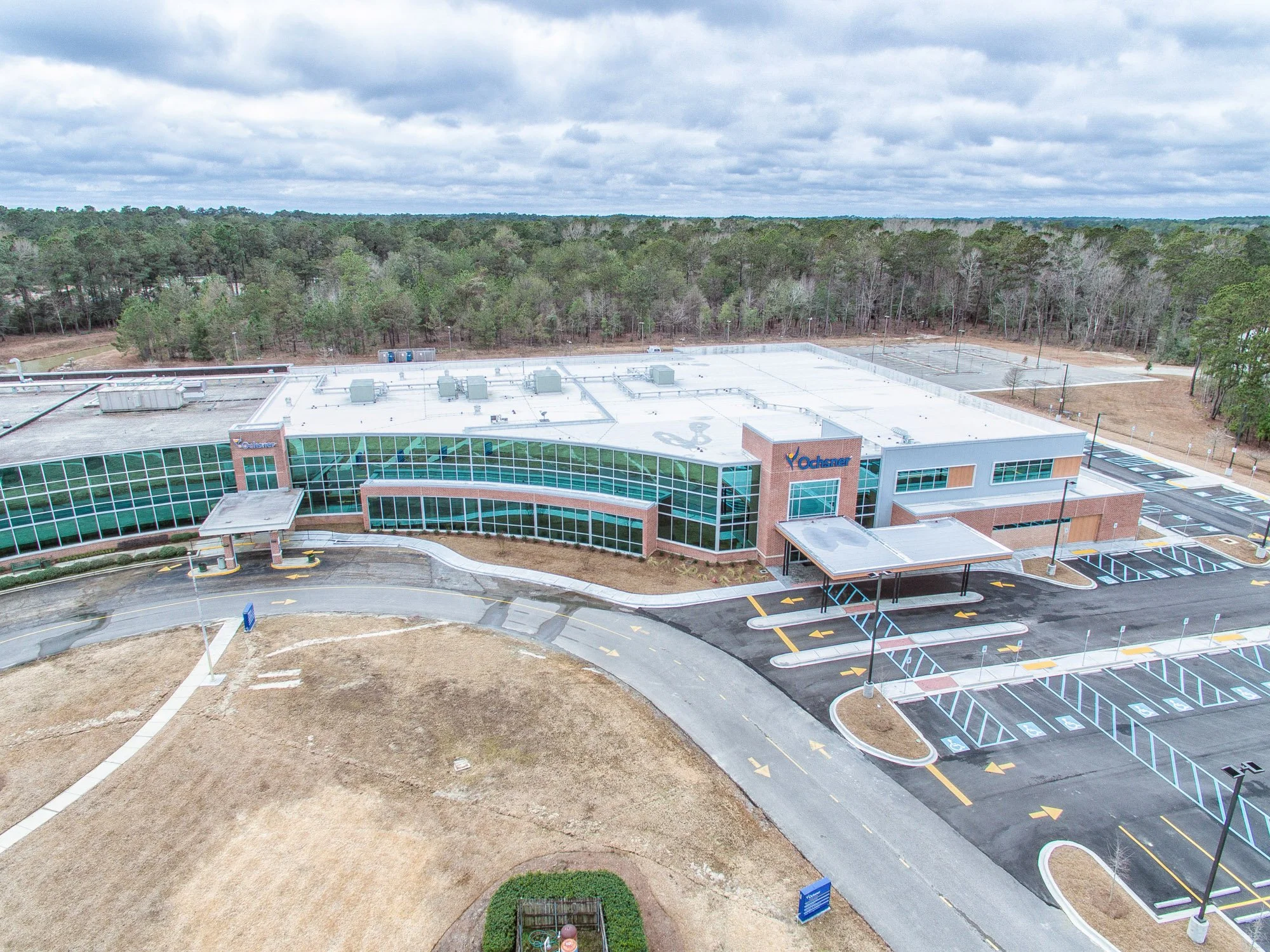 Aerial view of a modern office building with a parking lot, surrounded by trees and an open field.