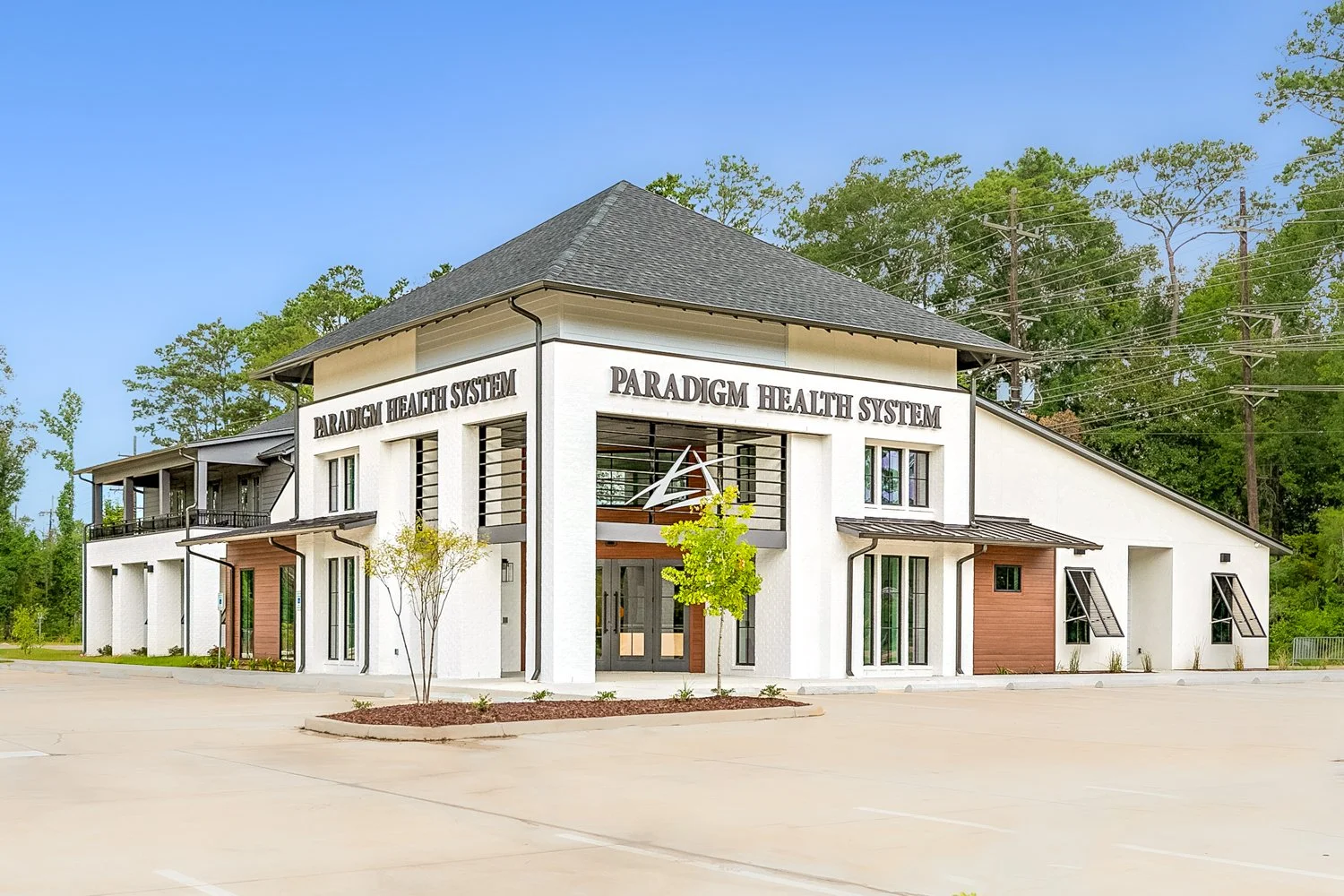 New multi-story health clinic building with the sign 'Paradigm Health System' on the front, surrounded by a large empty parking lot and trees in the background.