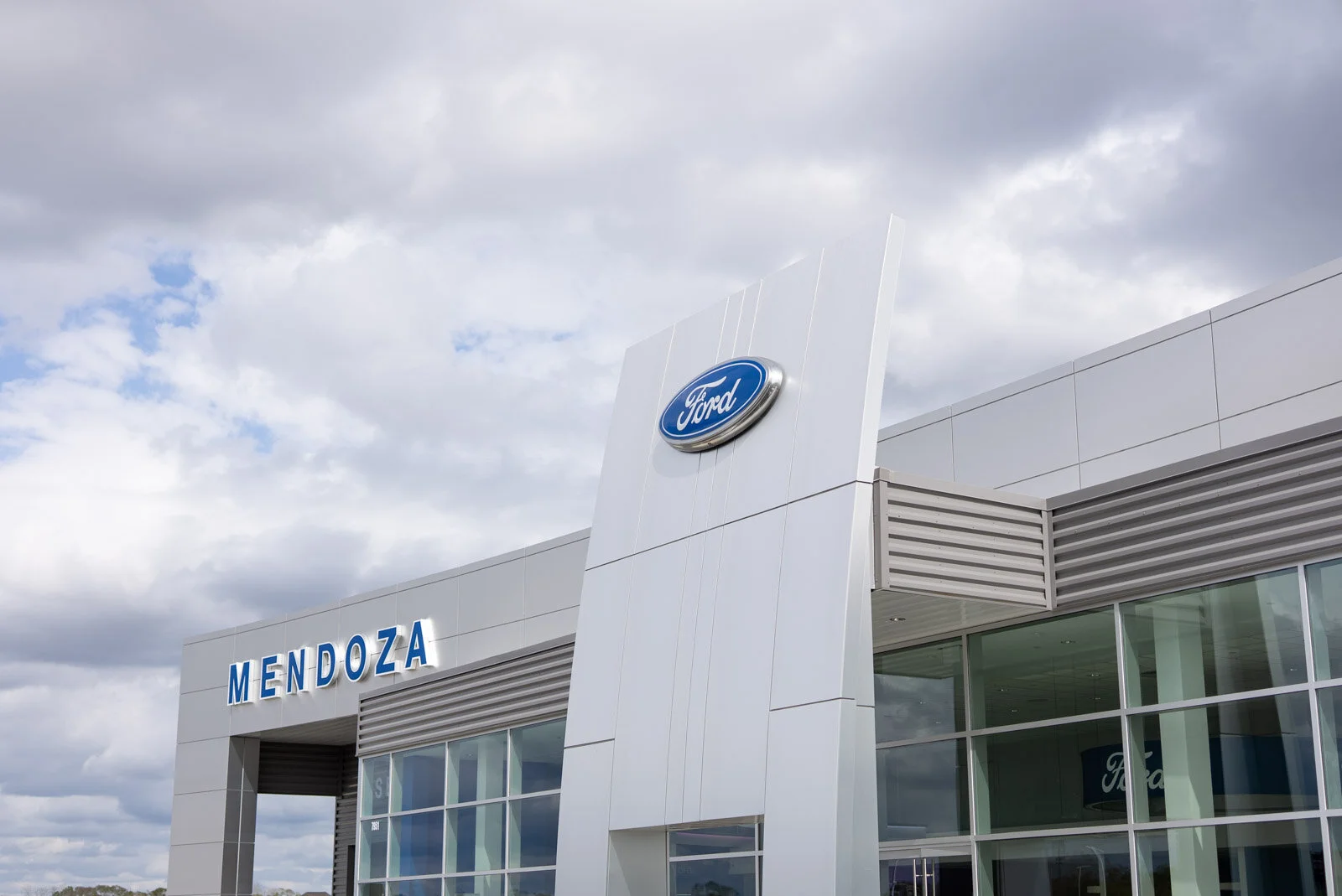 Ford dealership building with a sign that says Mendoza, under a partly cloudy sky.