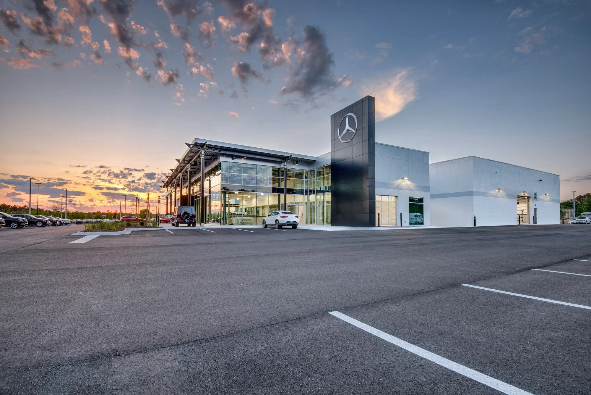 Mercedes-Benz dealership building at sunset with cars parked outside.