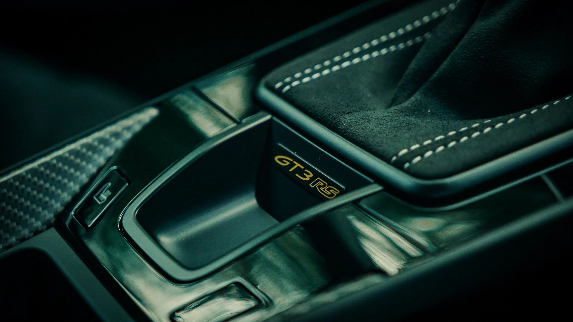 Close-up of a car's gear shift console with a GT3 RS badge, showing a suede shift boot and controlling buttons.